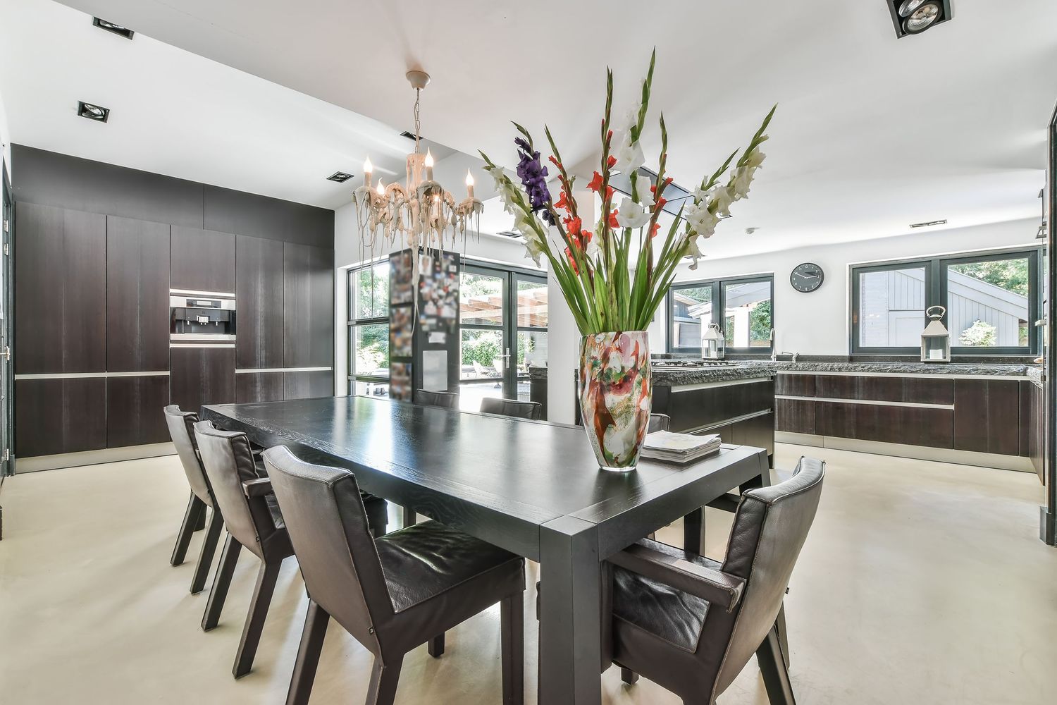 Modern dining room with dark wood table, leather chairs, and a floral centerpiece in an open-plan kitchen.