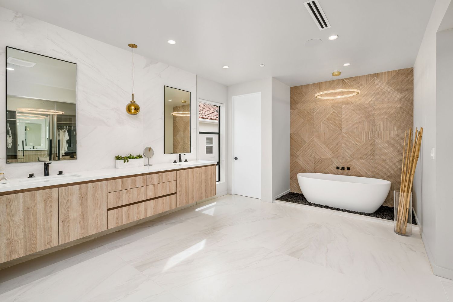 Modern luxury bathroom with floating wood vanity, marble walls, gold pendant lights, and freestanding soaking tub.