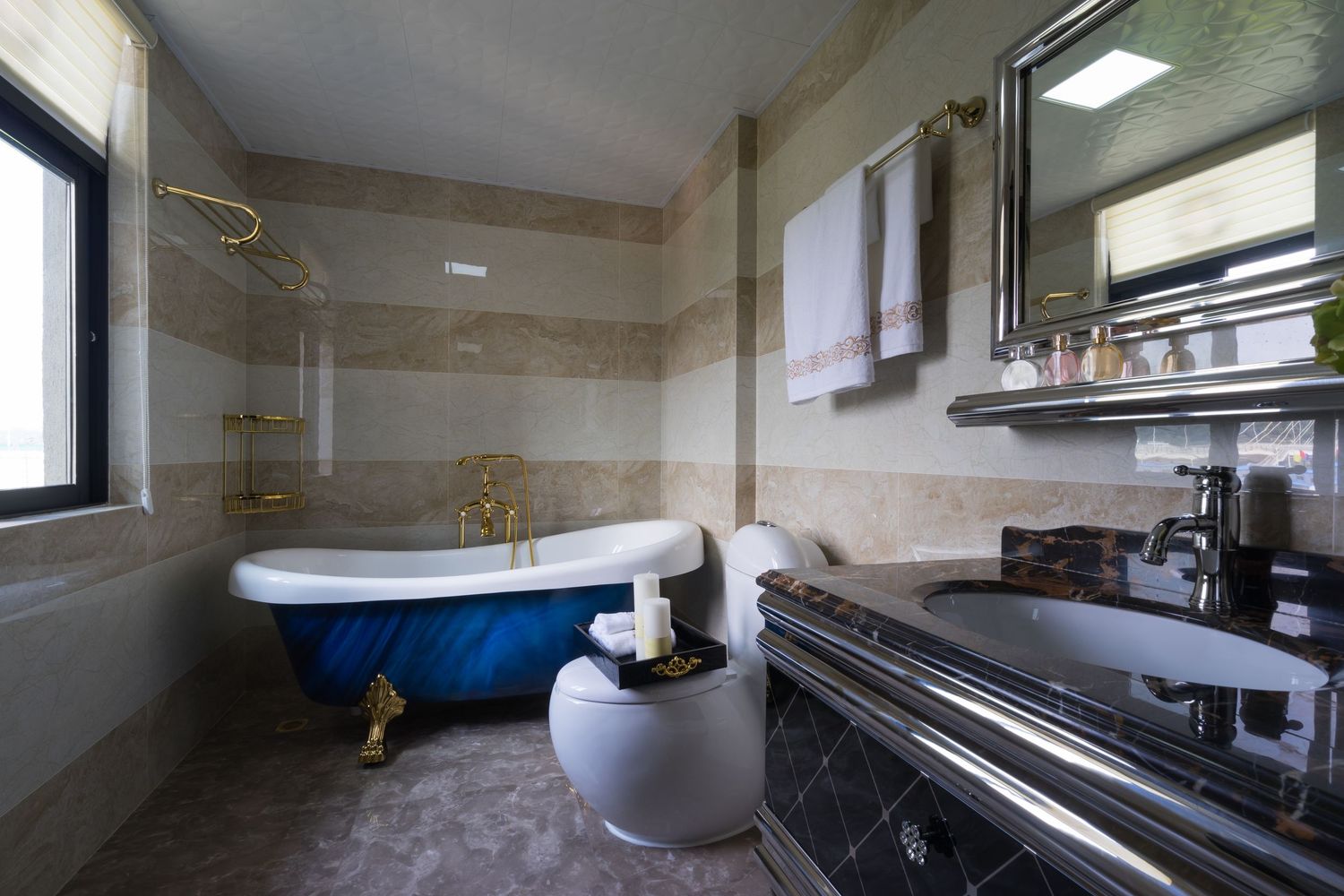 Luxury bathroom featuring a blue clawfoot bathtub with gold fixtures and marble walls.