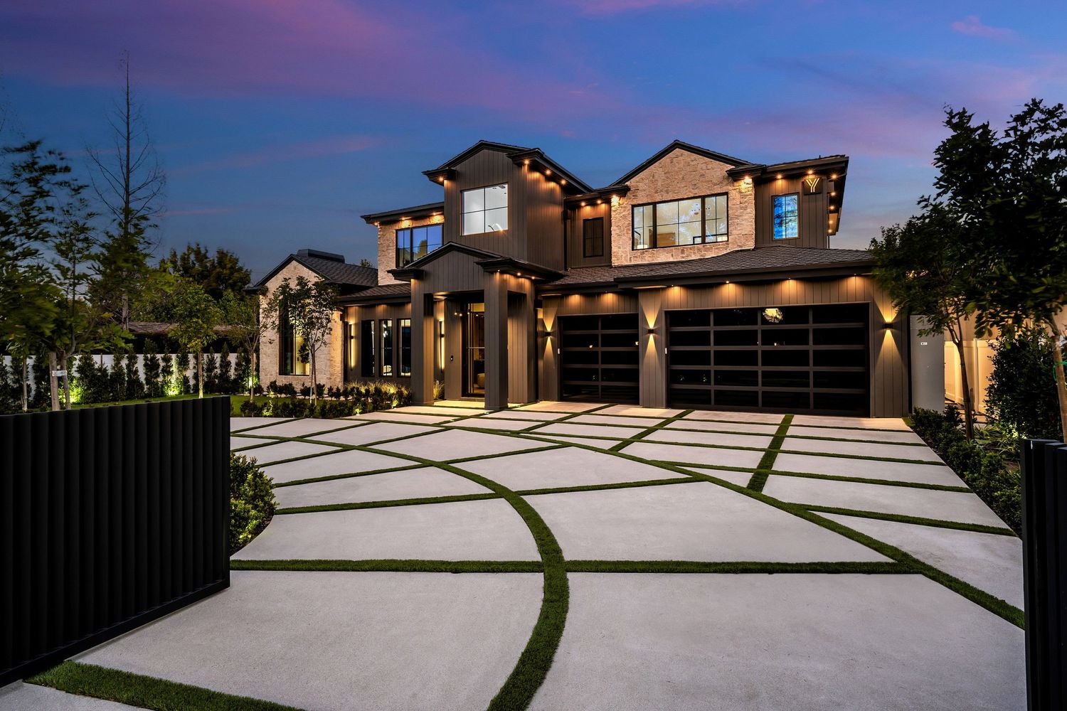 Luxury two-story home with geometric concrete driveway, glass garage doors, and elegant landscape lighting at dusk.
