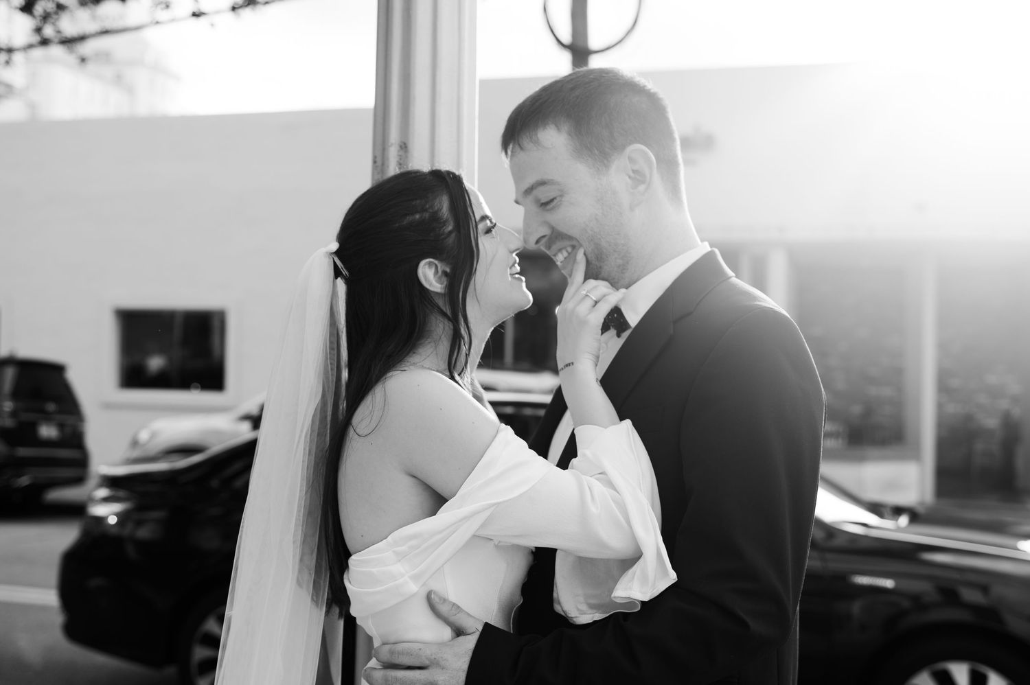 A black and white portrait of a bride and groom embracing and smiling at each other on a city street.