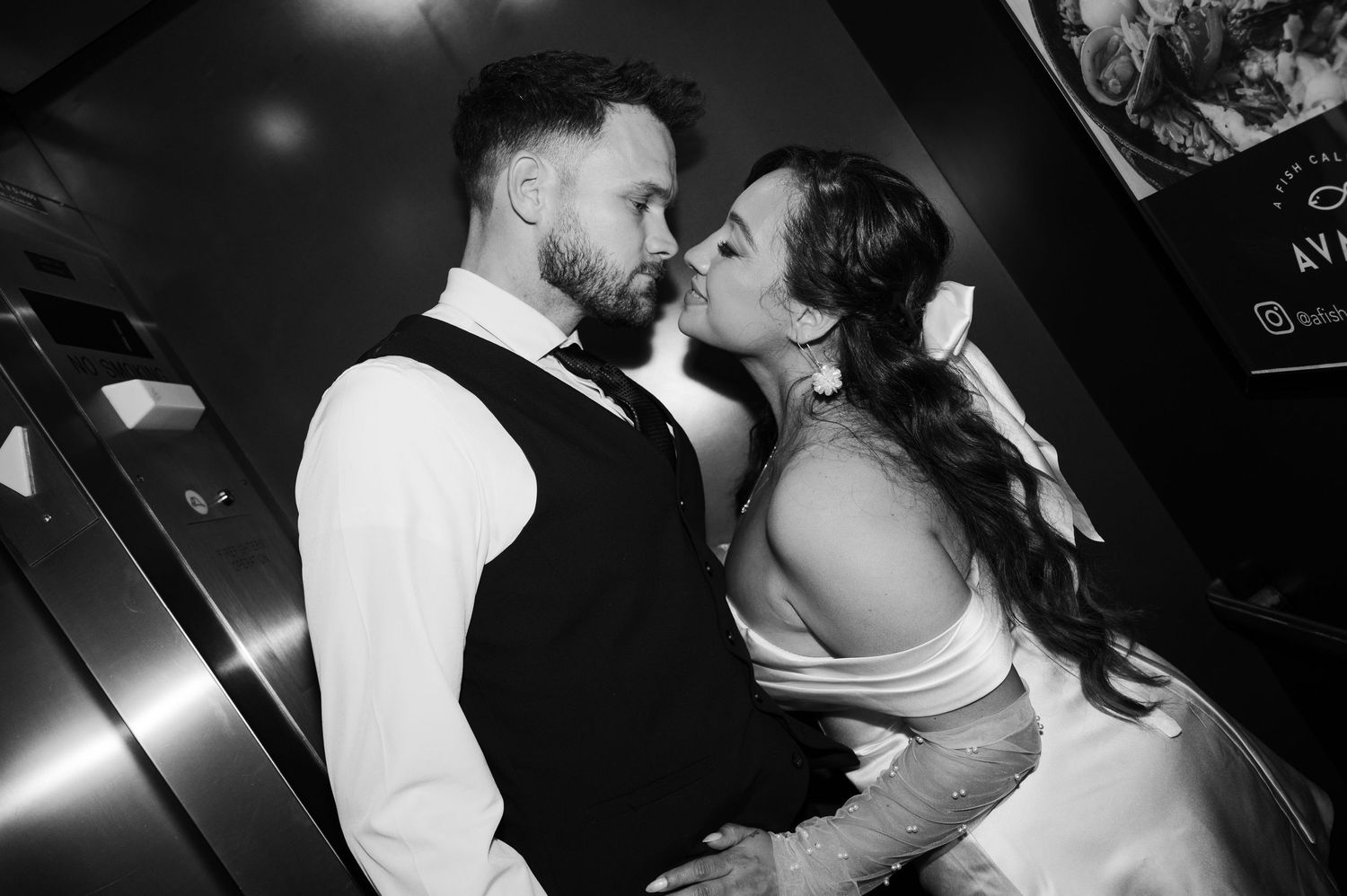Black and white photo of a bride and groom sharing a kiss, the groom in a vest and the bride in lace gloves.