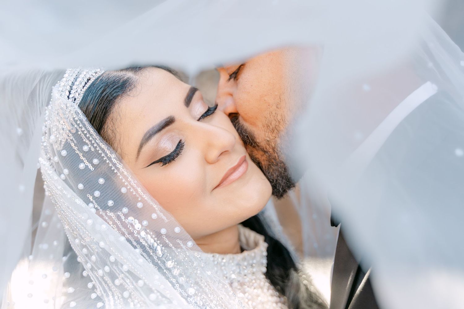 Groom kissing the bride's forehead beneath her veil.