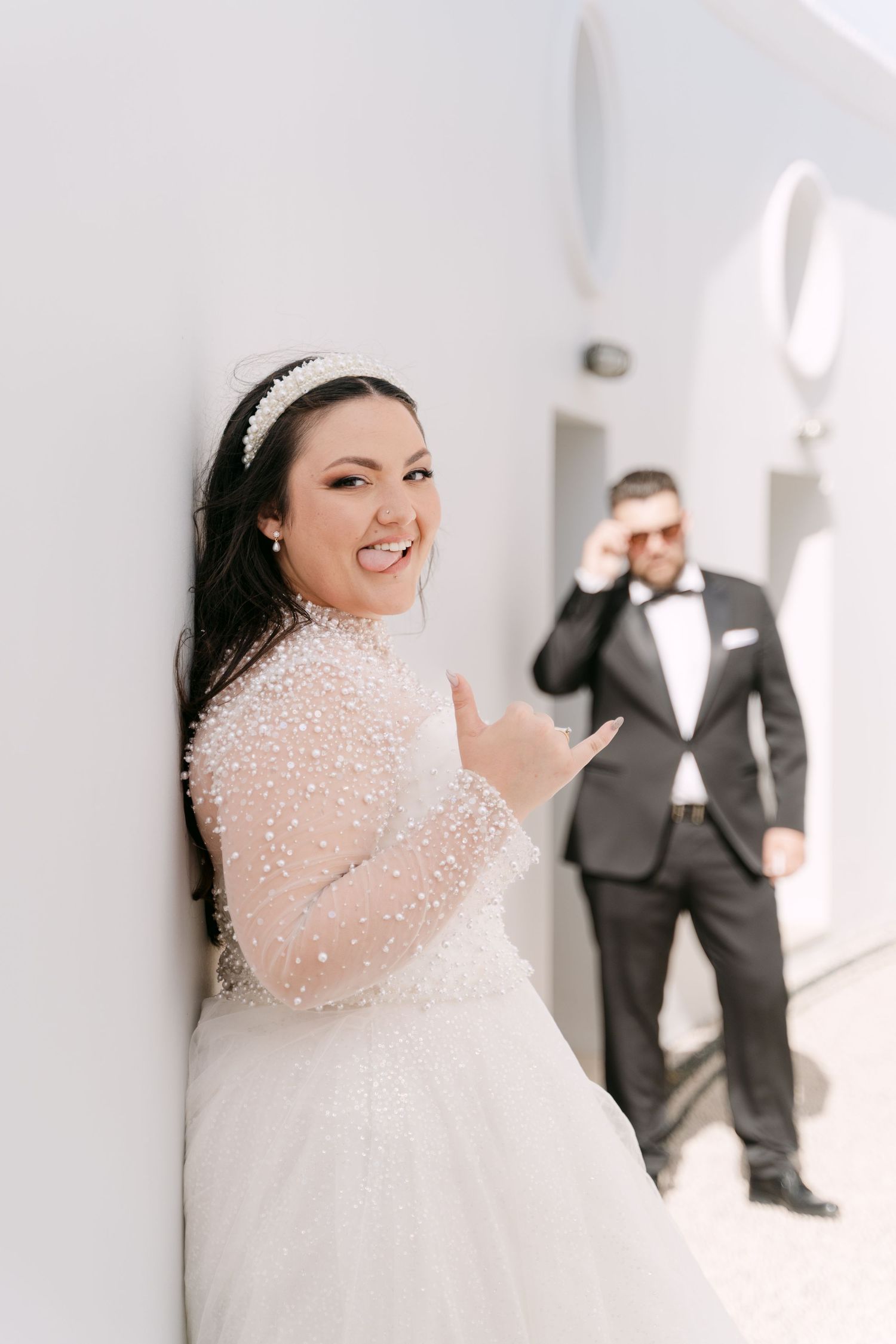 Bride smiling in a sunlit whitewashed lane with the groom in the background.