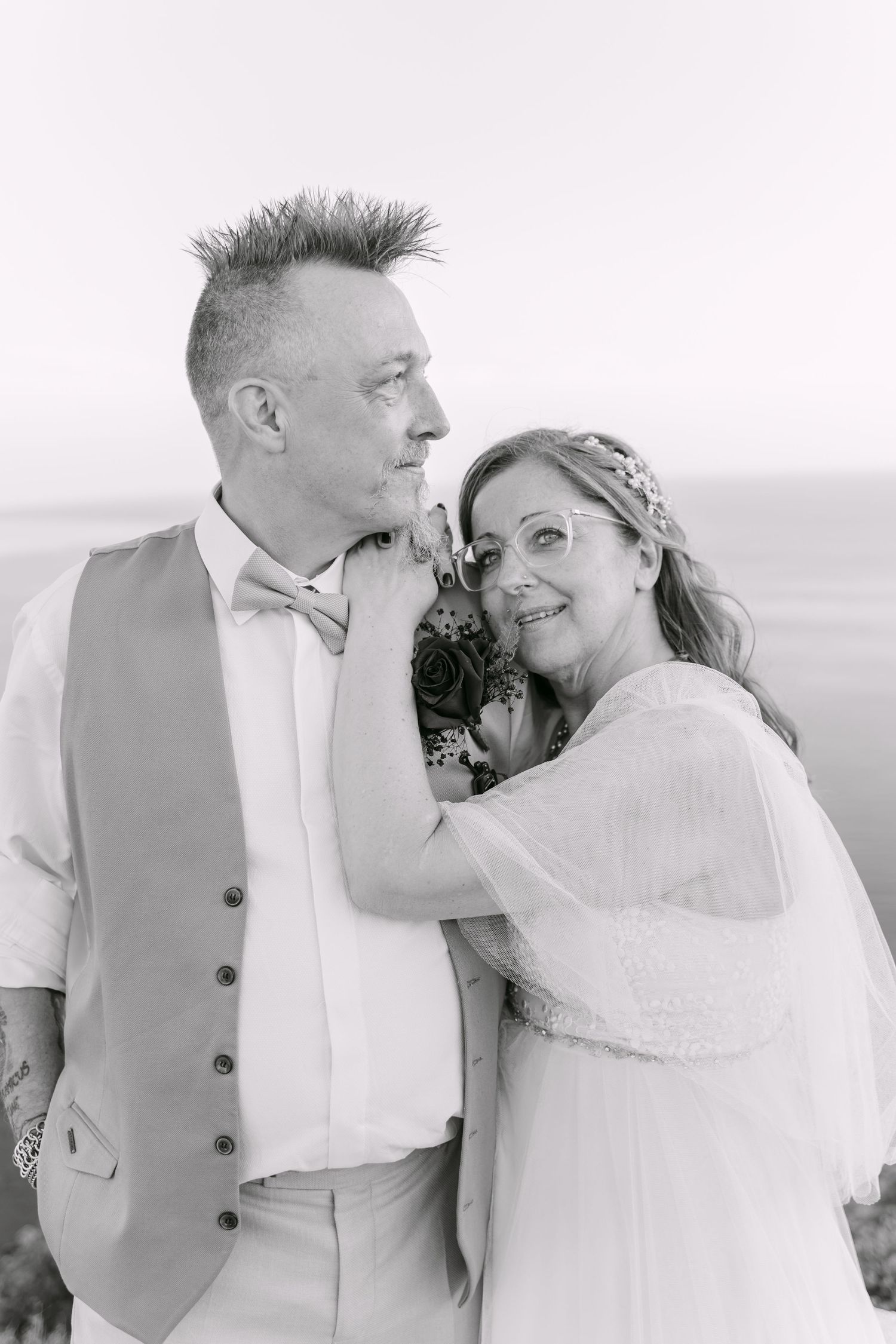 Black and white portrait of a couple smiling together by the sea.