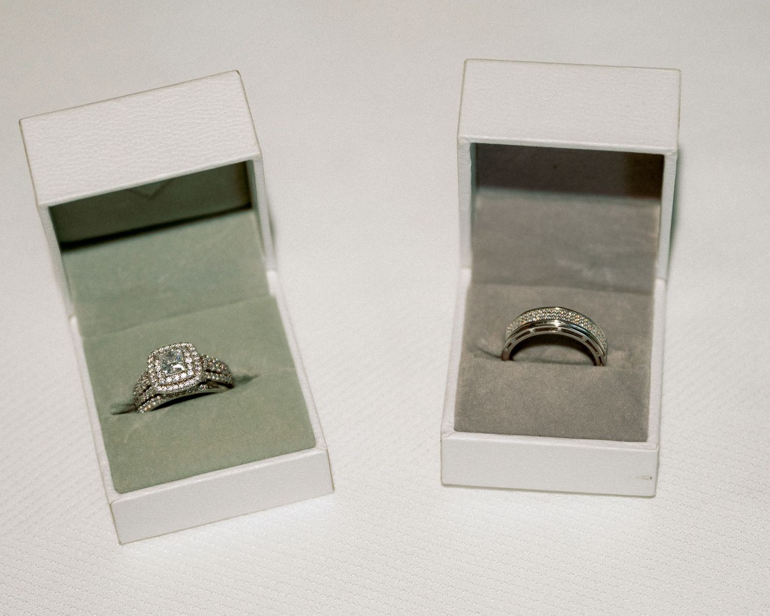 Two diamond wedding ring sets displayed in white jewelry boxes, featuring halo engagement ring and matching band in white gold.