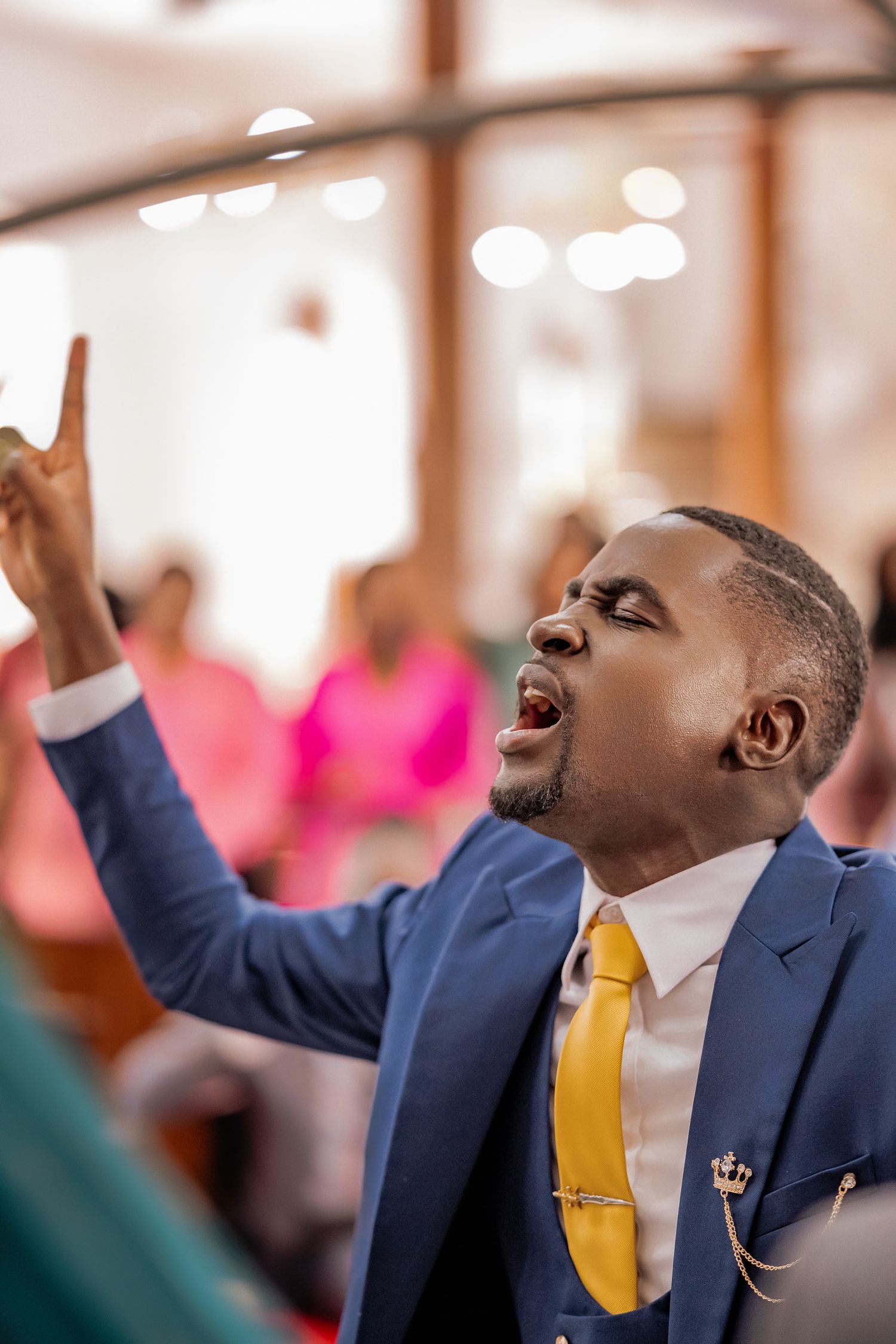 A man in a blue suit and gold tie raises his finger and sings passionately during a church wedding ceremony.