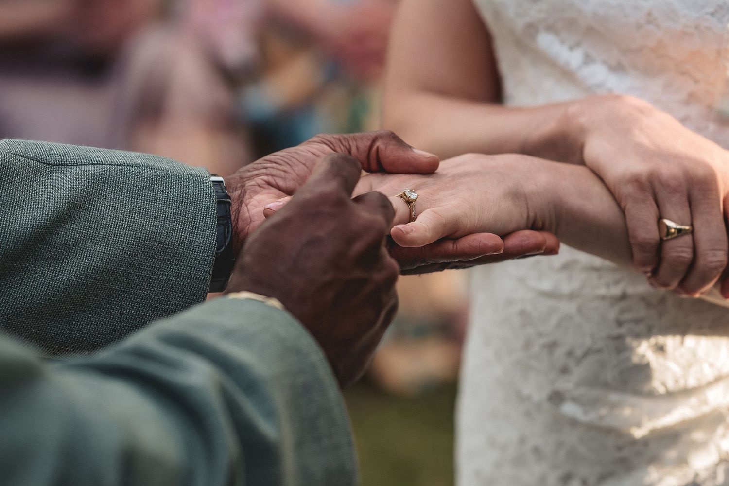 Close-up of groom placing wedding ring on bride's finger during outdoor marriage ceremony.