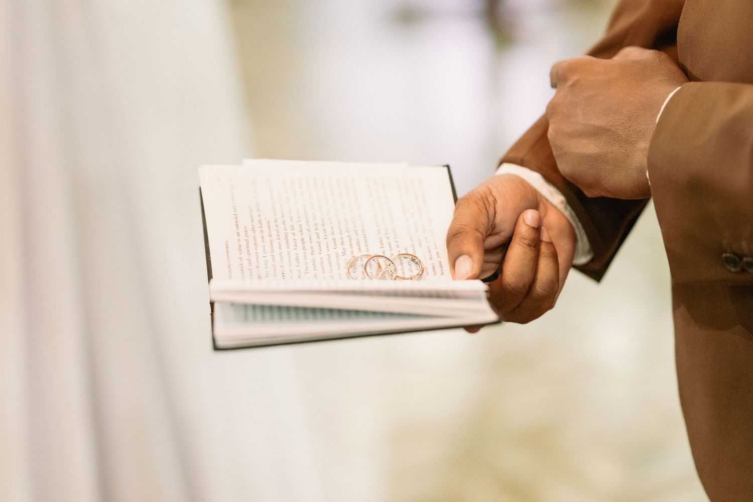 Officiant holds open book with two gold wedding rings resting on pages during wedding ceremony.
