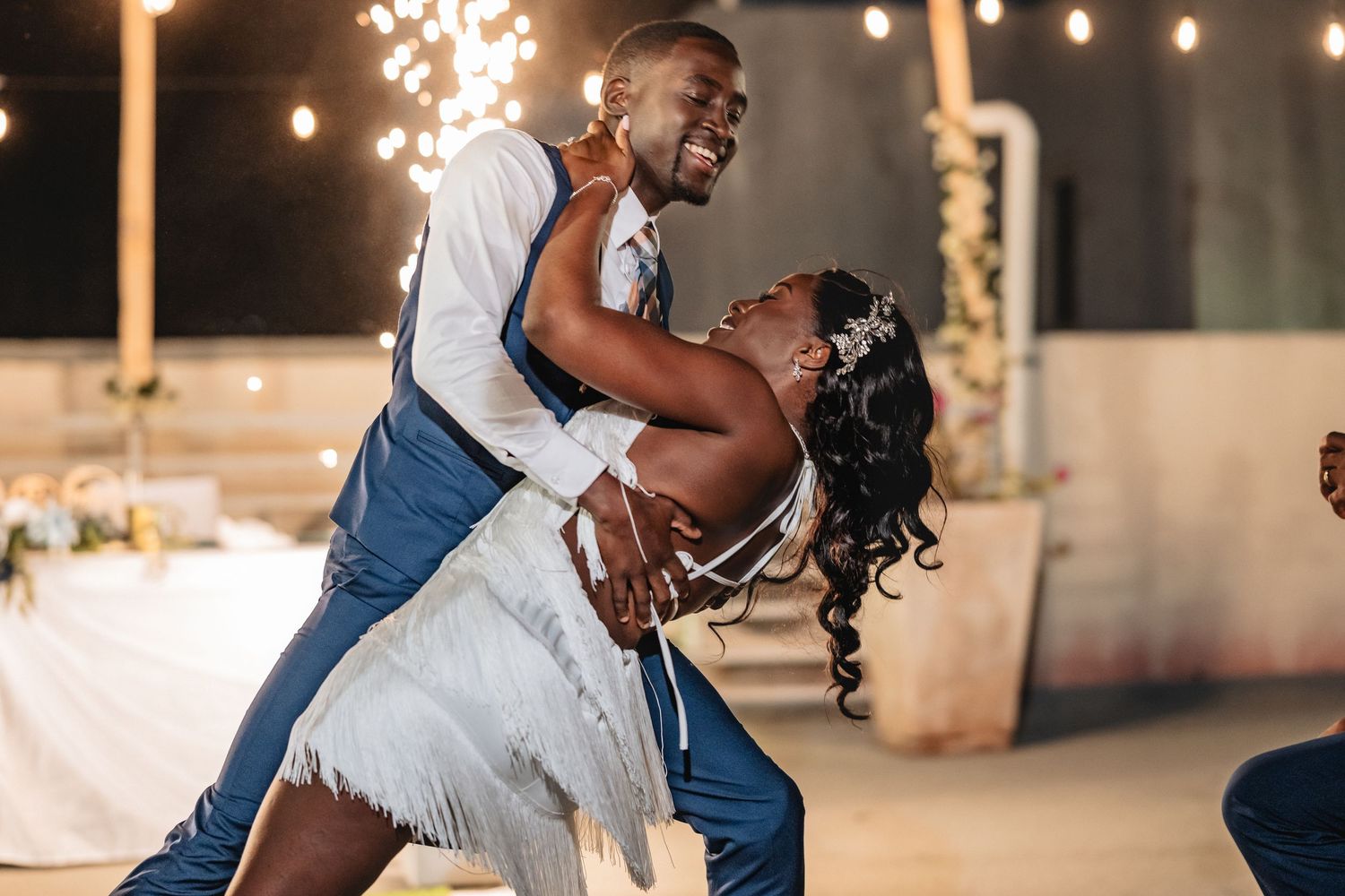 Joyful bride and groom sharing romantic first dance dip under sparkling lights at wedding reception.