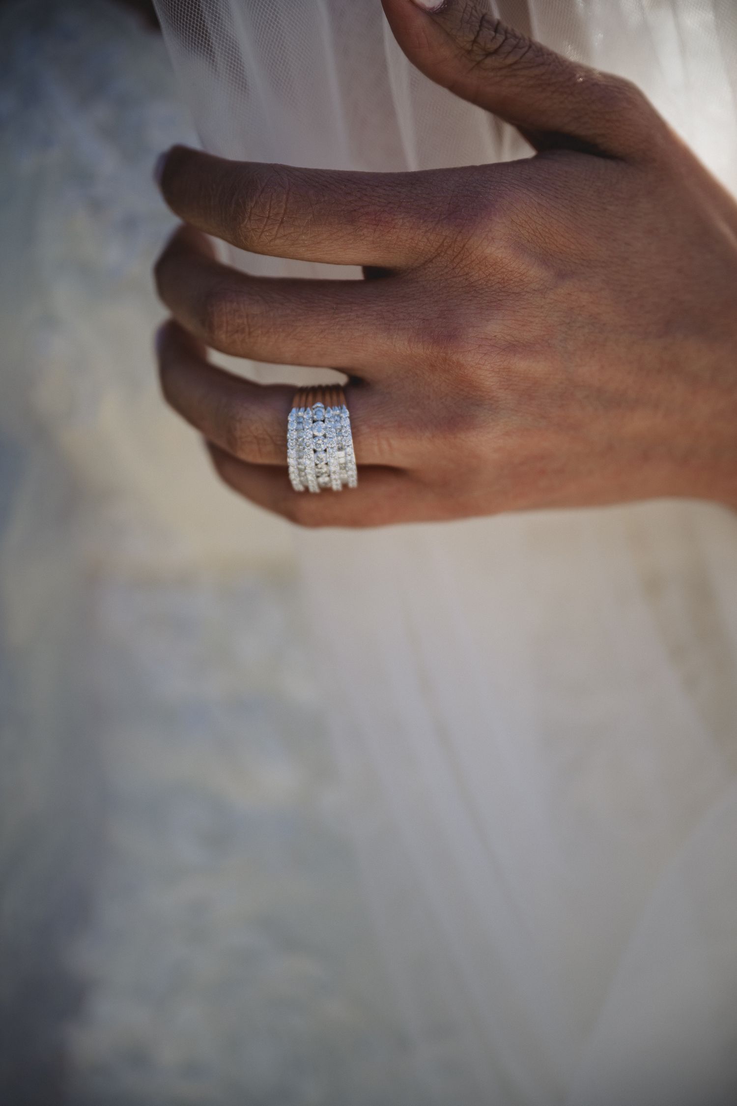 Close-up of stacked diamond wedding rings on a dark-skinned hand against a white wedding dress.