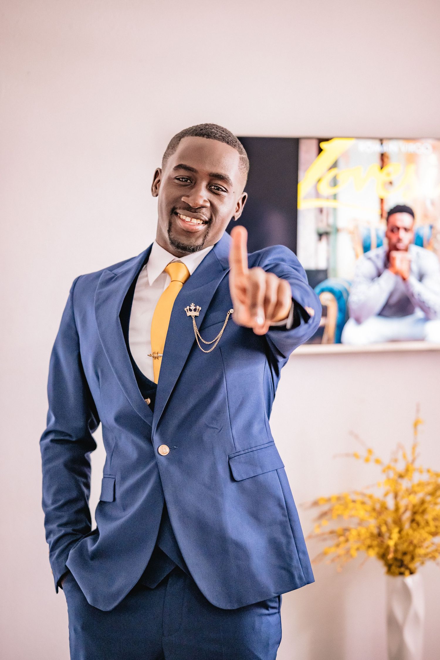 Groom wearing navy blue suit with yellow tie poses confidently indoors.