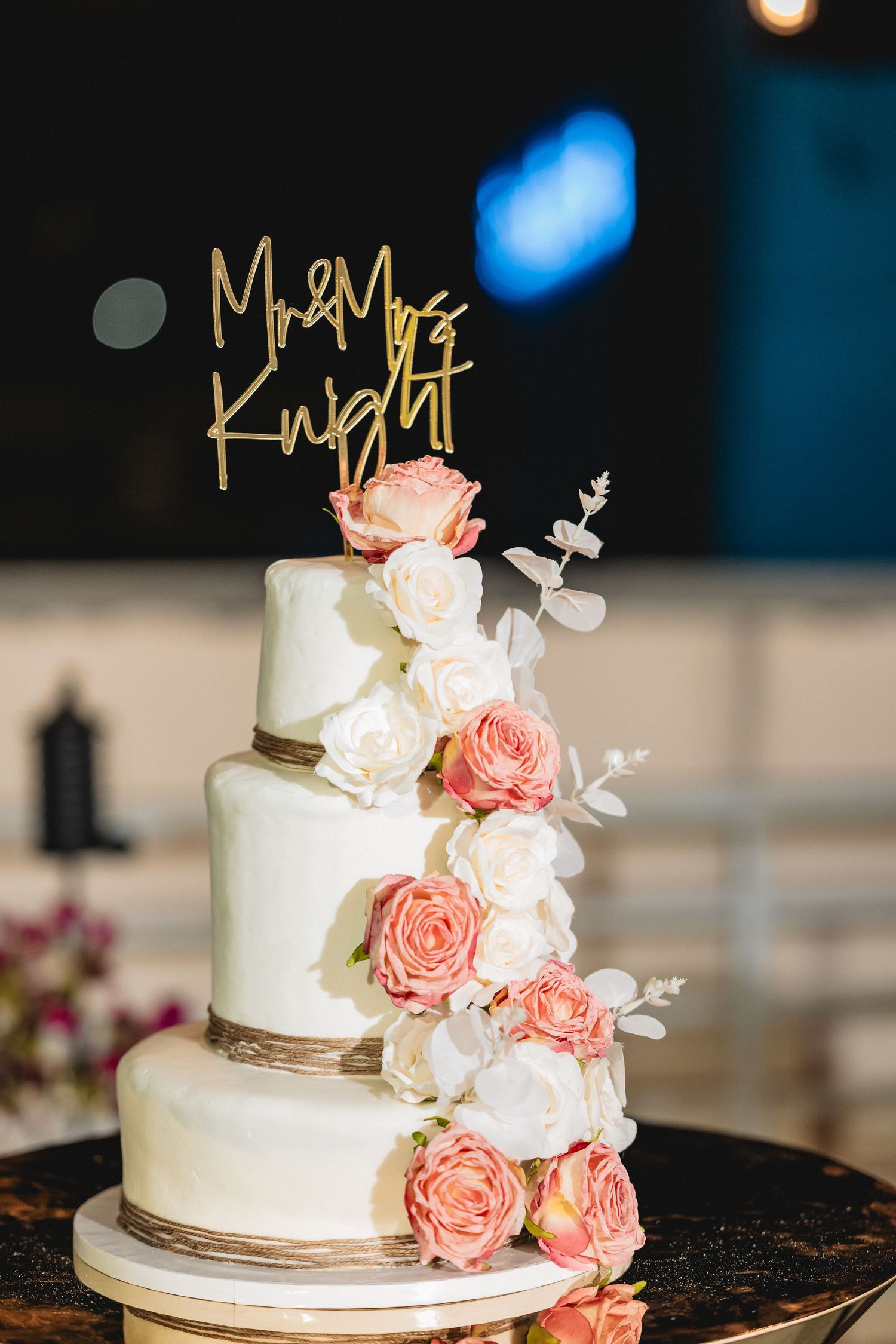 Elegant white wedding cake decorated with peach roses and gold Mr & Mrs topper.