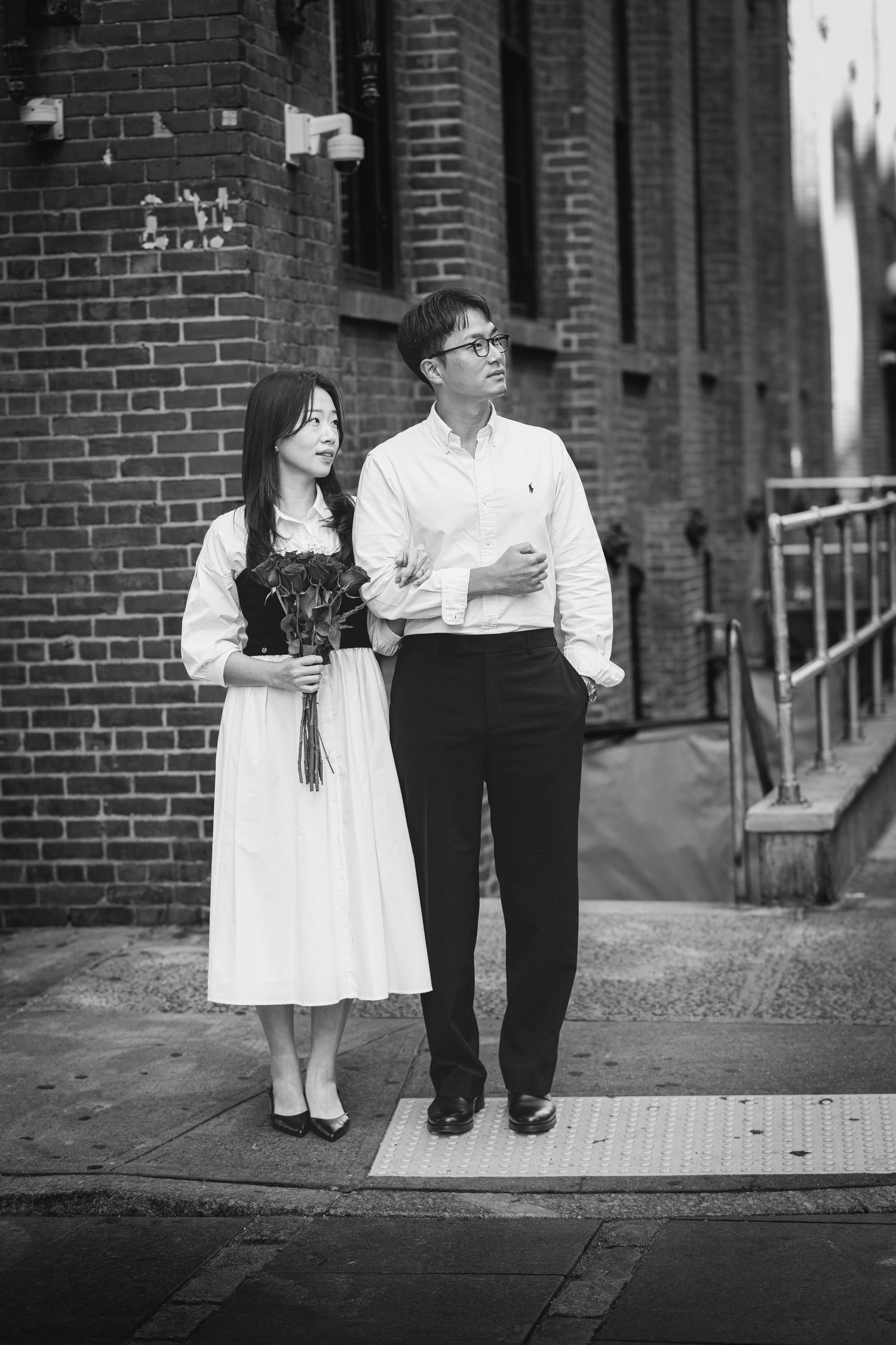 A romantic black and white engagement photo series against a brick wall backdrop.