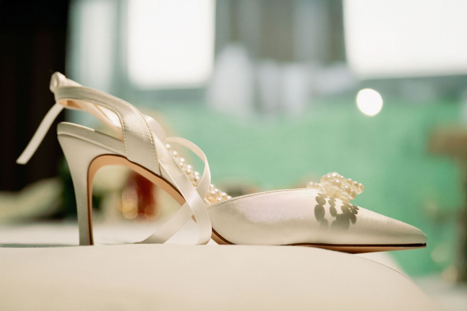 Elegant white bridal heels with pearl embellishments displayed on a reflective surface.