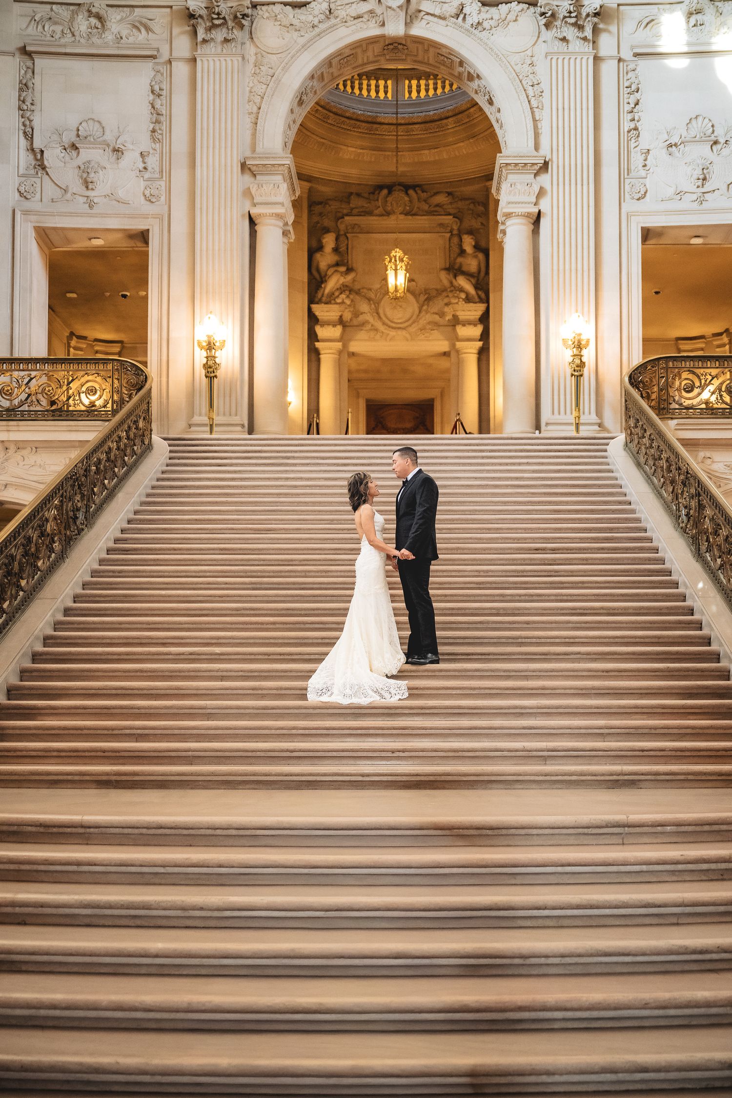 Bride and groom holding hands on grand marble staircase at San Francisco City Hall wedding ceremony.