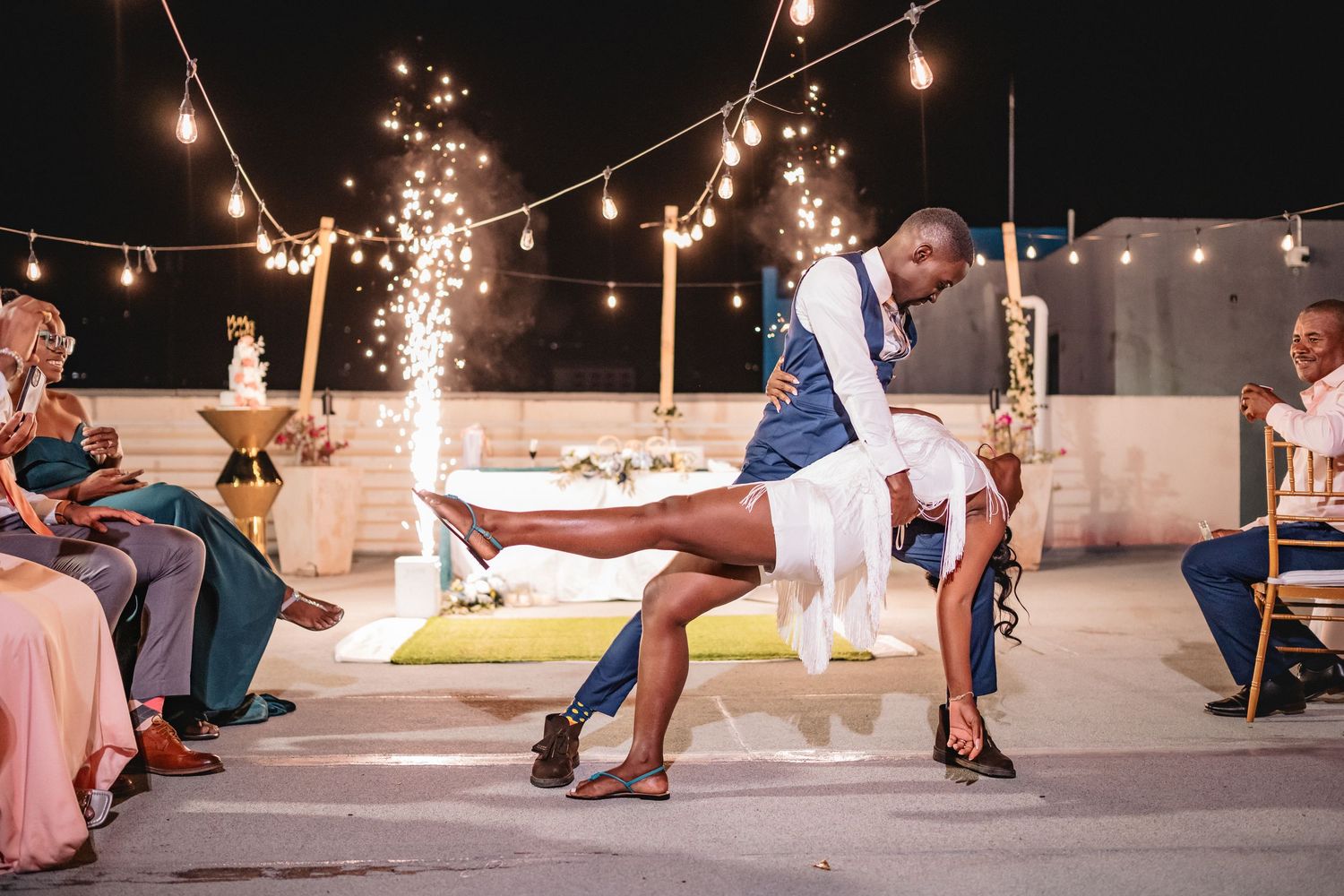 Couple sharing a romantic dip dance at an outdoor wedding reception under string lights at night.