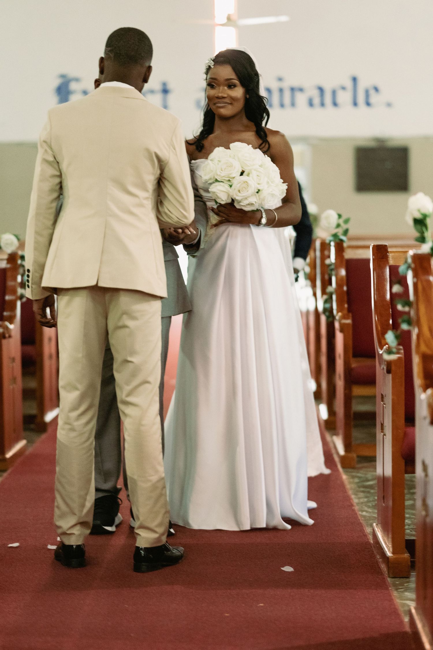 Bride and groom walking down church aisle during wedding ceremony, bride holding white bouquet.