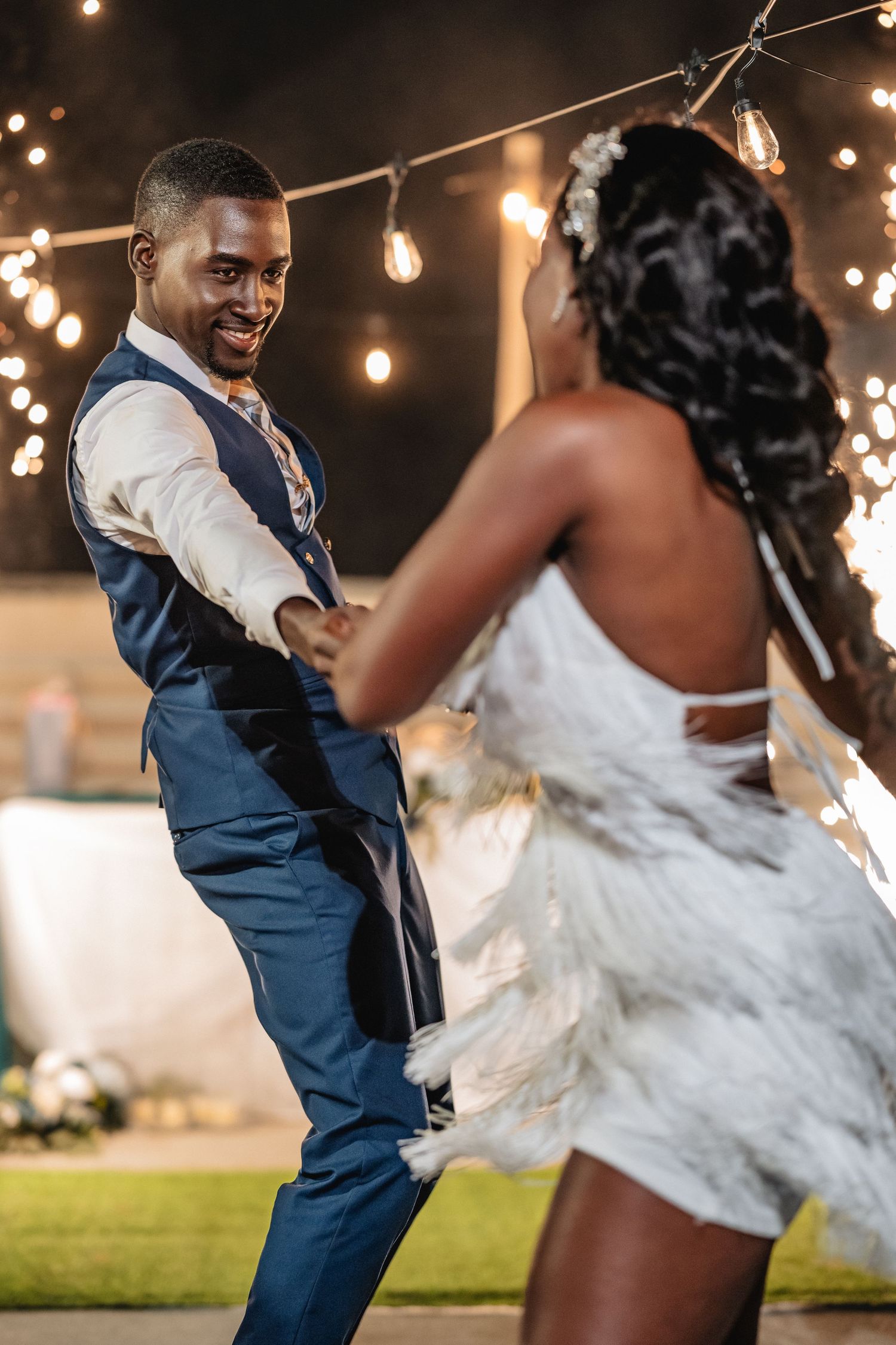 Joyful bride and groom share first dance under string lights at outdoor evening wedding reception.