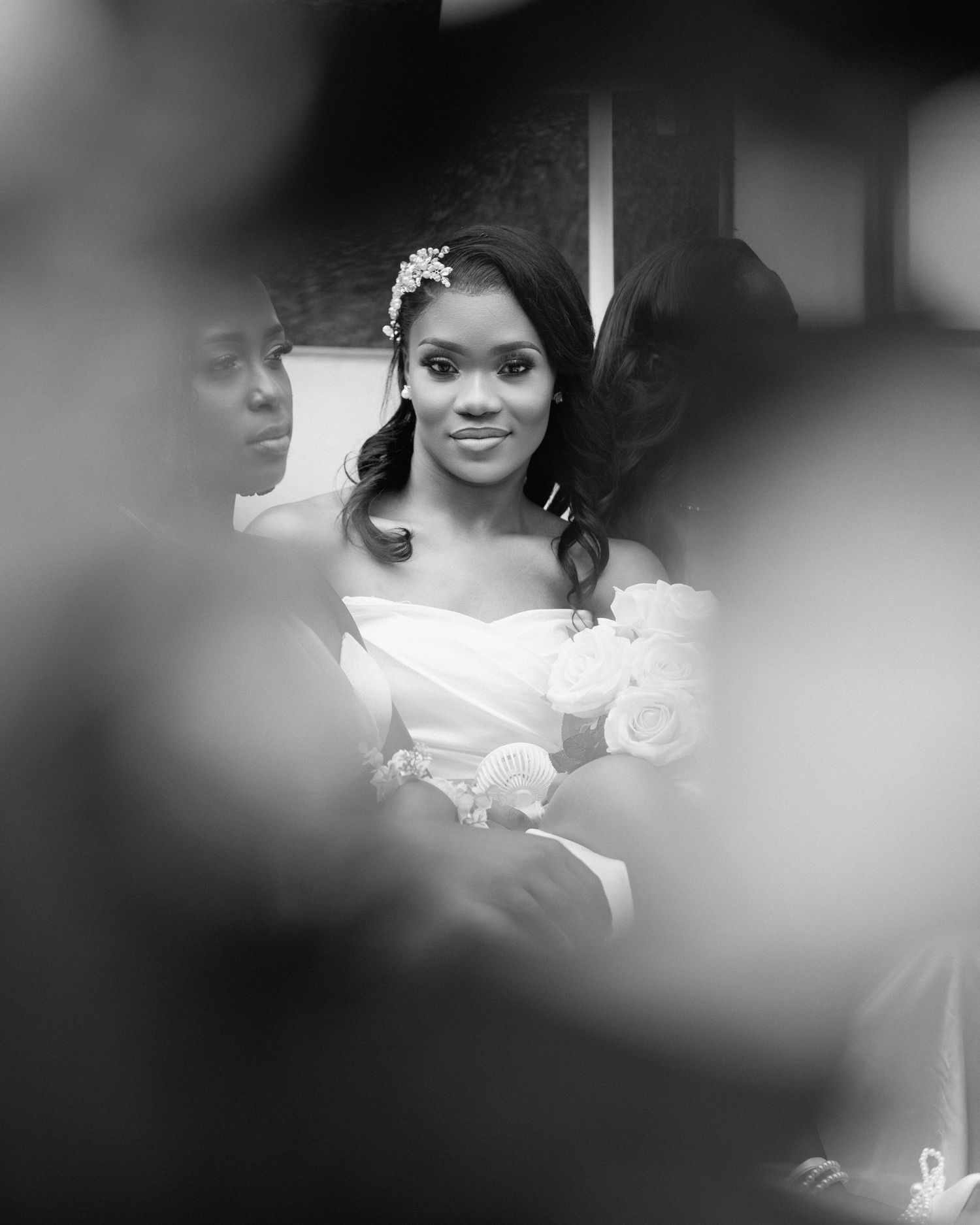 Elegant Black bride in off-shoulder wedding gown with floral headpiece captured through a soft bokeh frame.