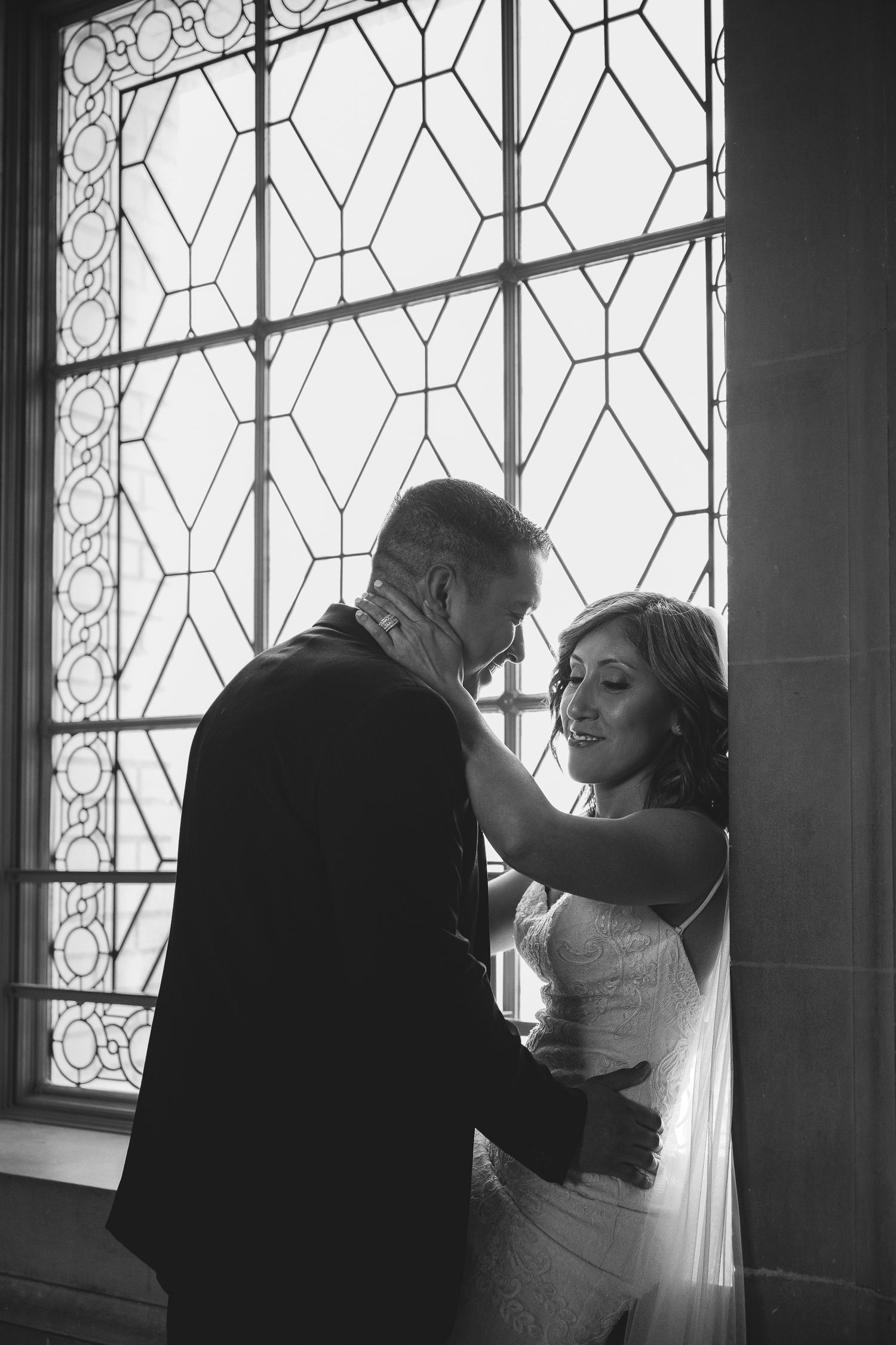 Black and white photo of bride and groom sharing intimate moment in front of ornate stained glass window.
