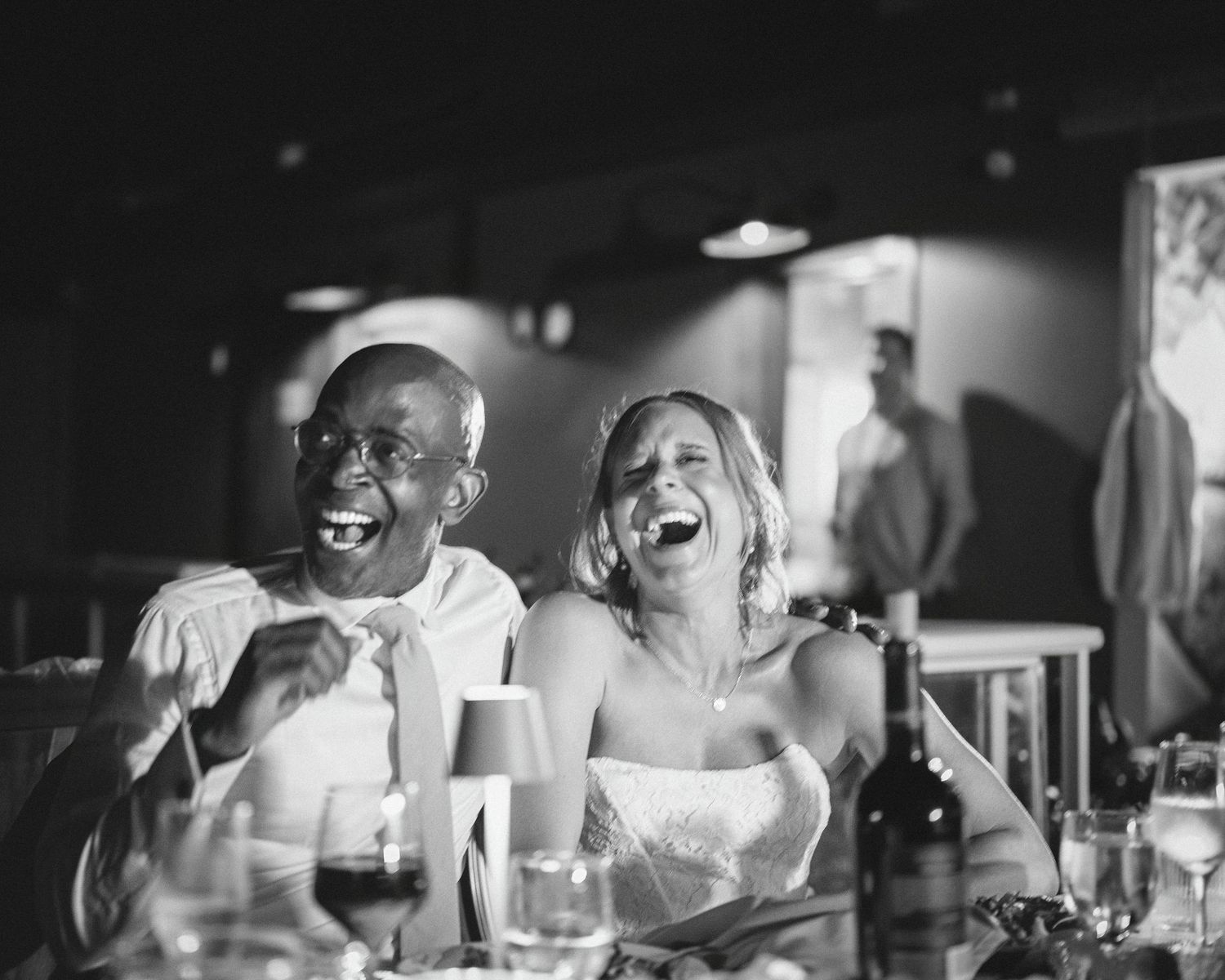 Black and white photo of a laughing bride and groom sharing a joyful moment at their wedding reception.
