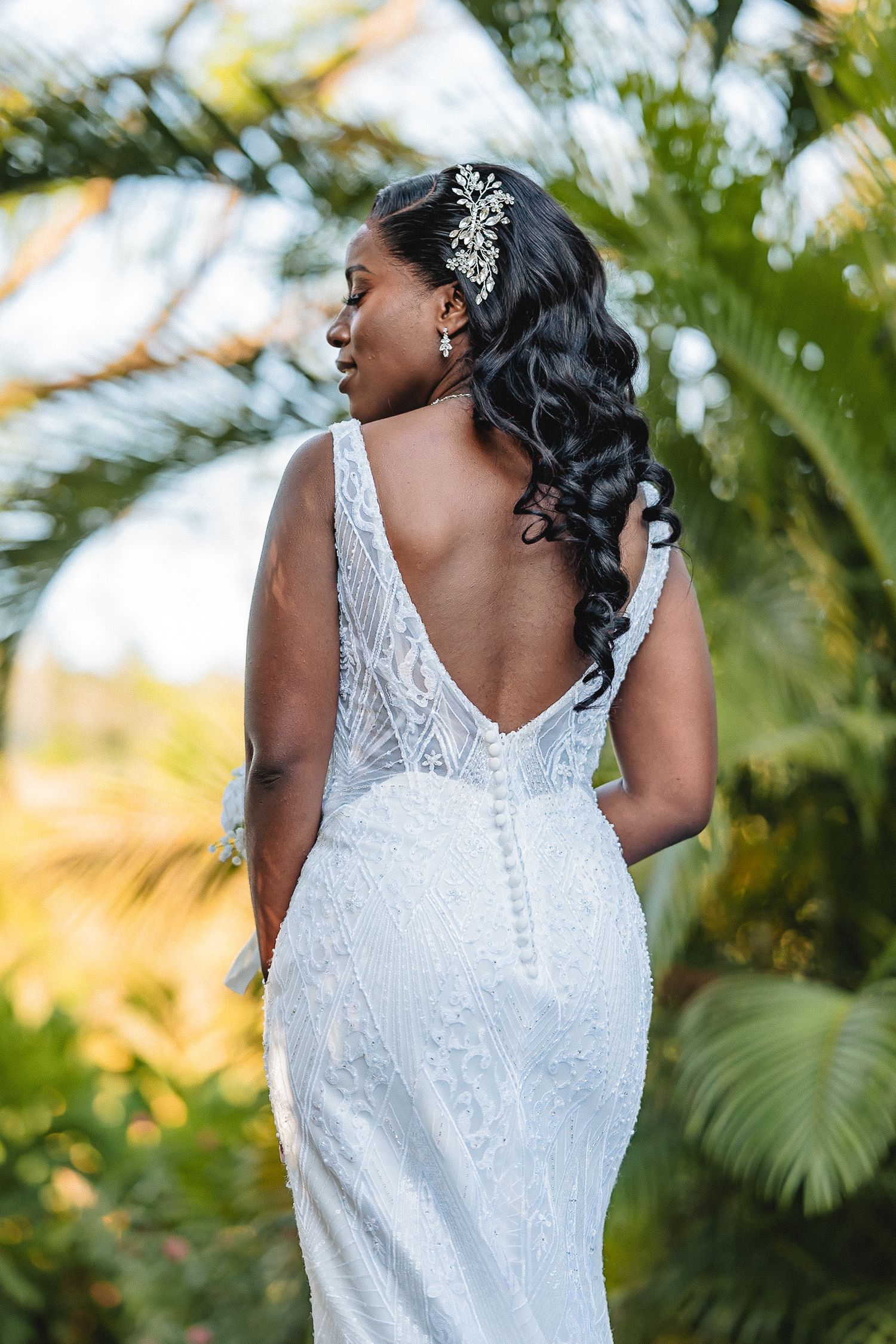 Back details of a white lace wedding dress with delicate straps against a tropical background.