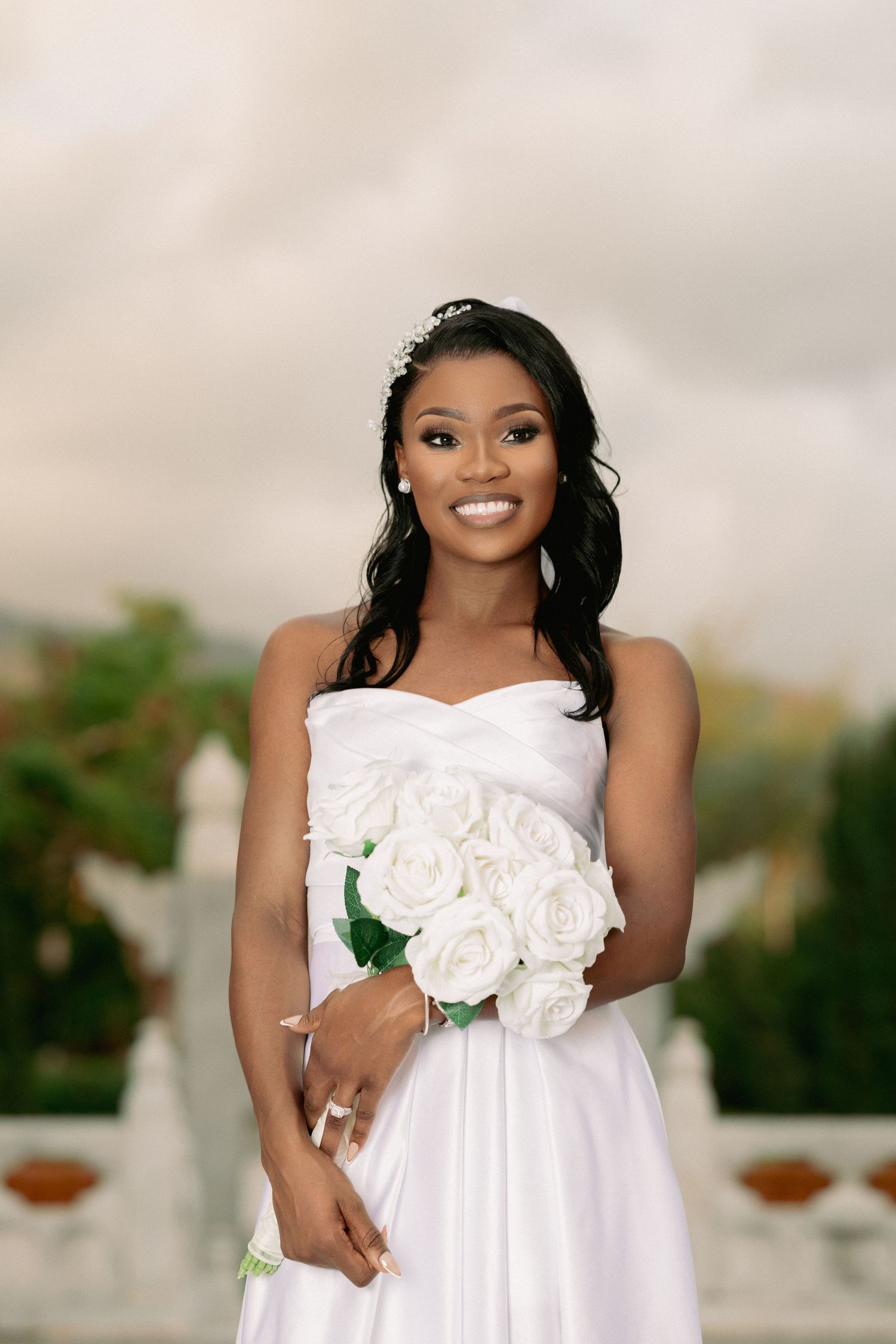 Bride in a white strapless wedding dress with white rose bouquet poses elegantly outdoors.