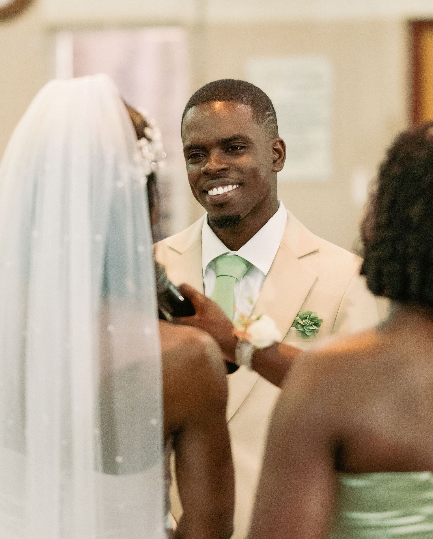 Smiling groom in beige suit with green tie during wedding ceremony at the altar.