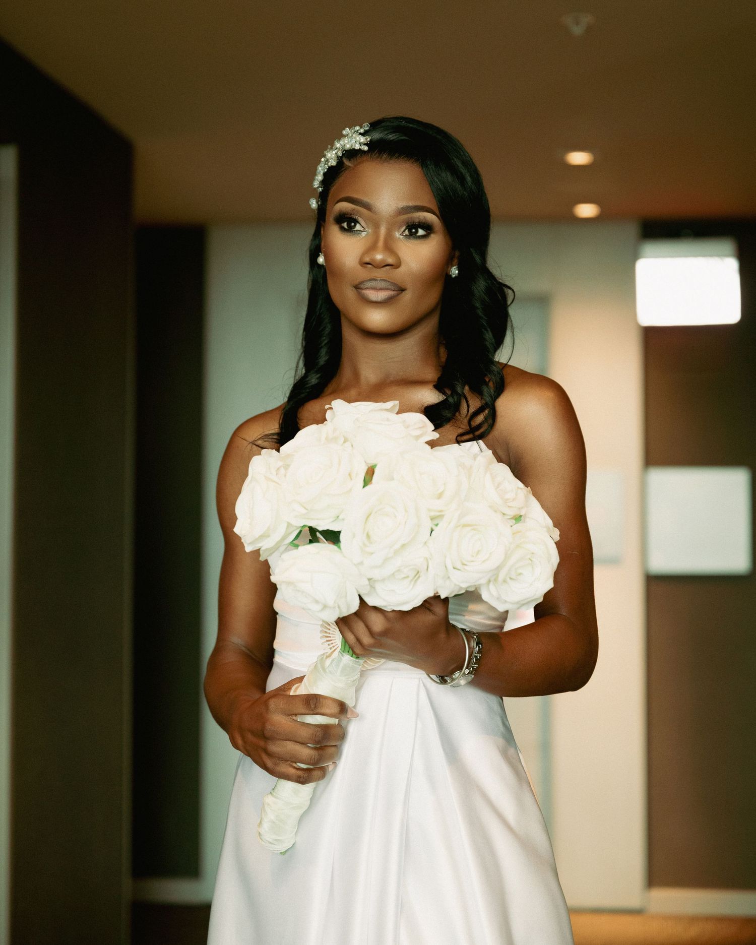 Elegant Black bride in white strapless gown holding bouquet of white roses with crystal hair accessory.