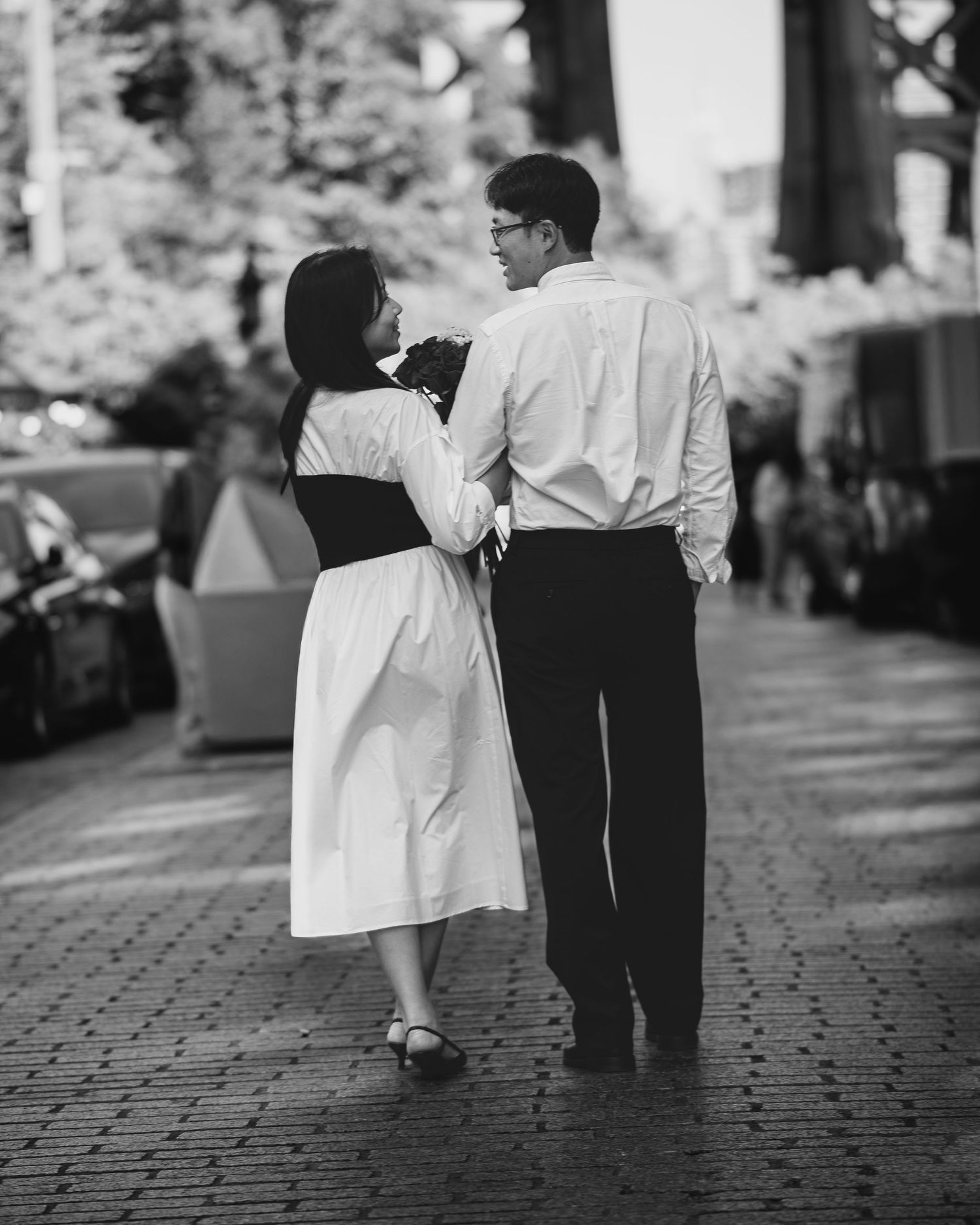 Candid black and white photos of a couple strolling together on a brick-paved path.