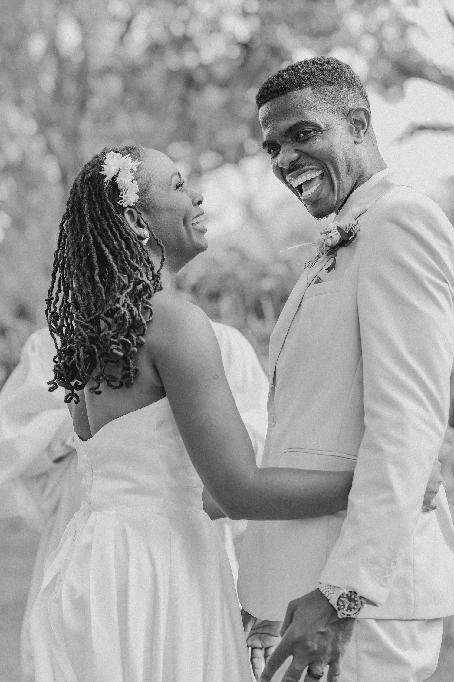 Joyful couple in white attire share candid laughs during outdoor photo session.