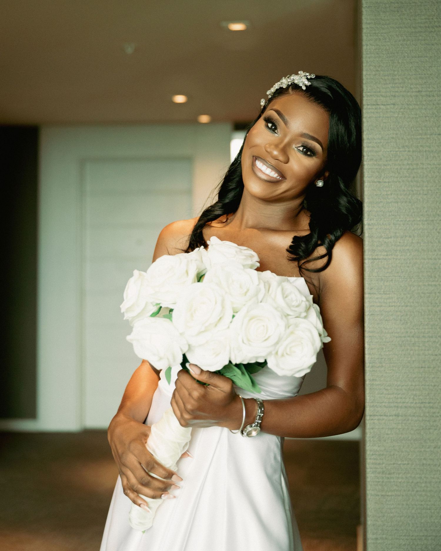 Radiant Black bride in a strapless white gown holding a bouquet of white roses on her wedding day.