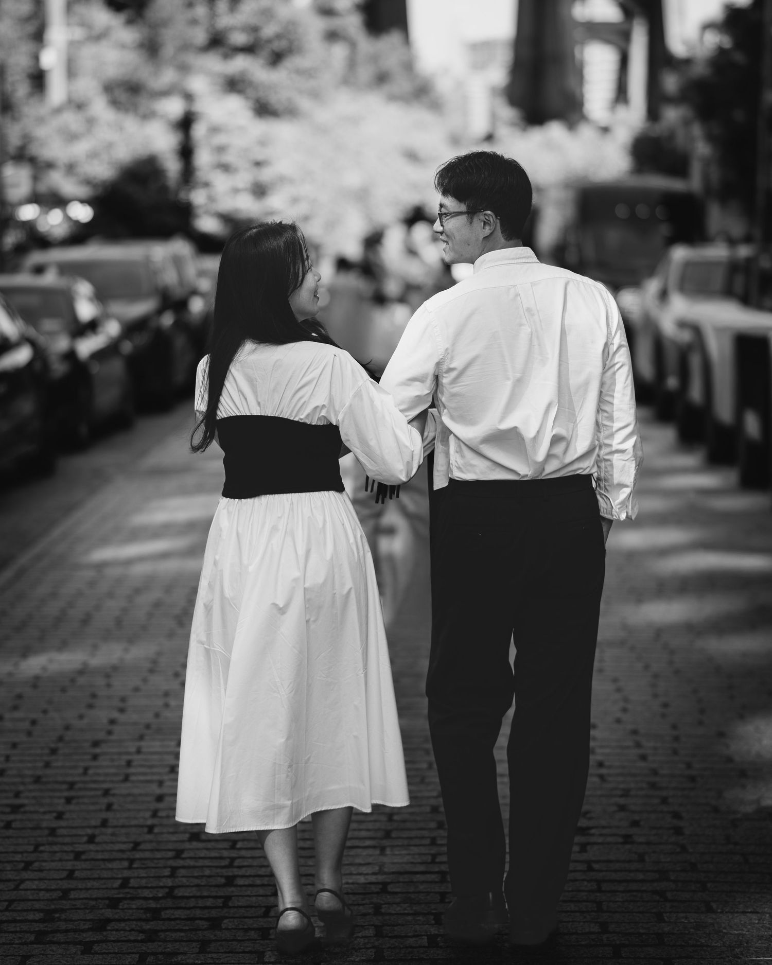 Couple walking hand in hand down a cobblestone street in black and white photography.