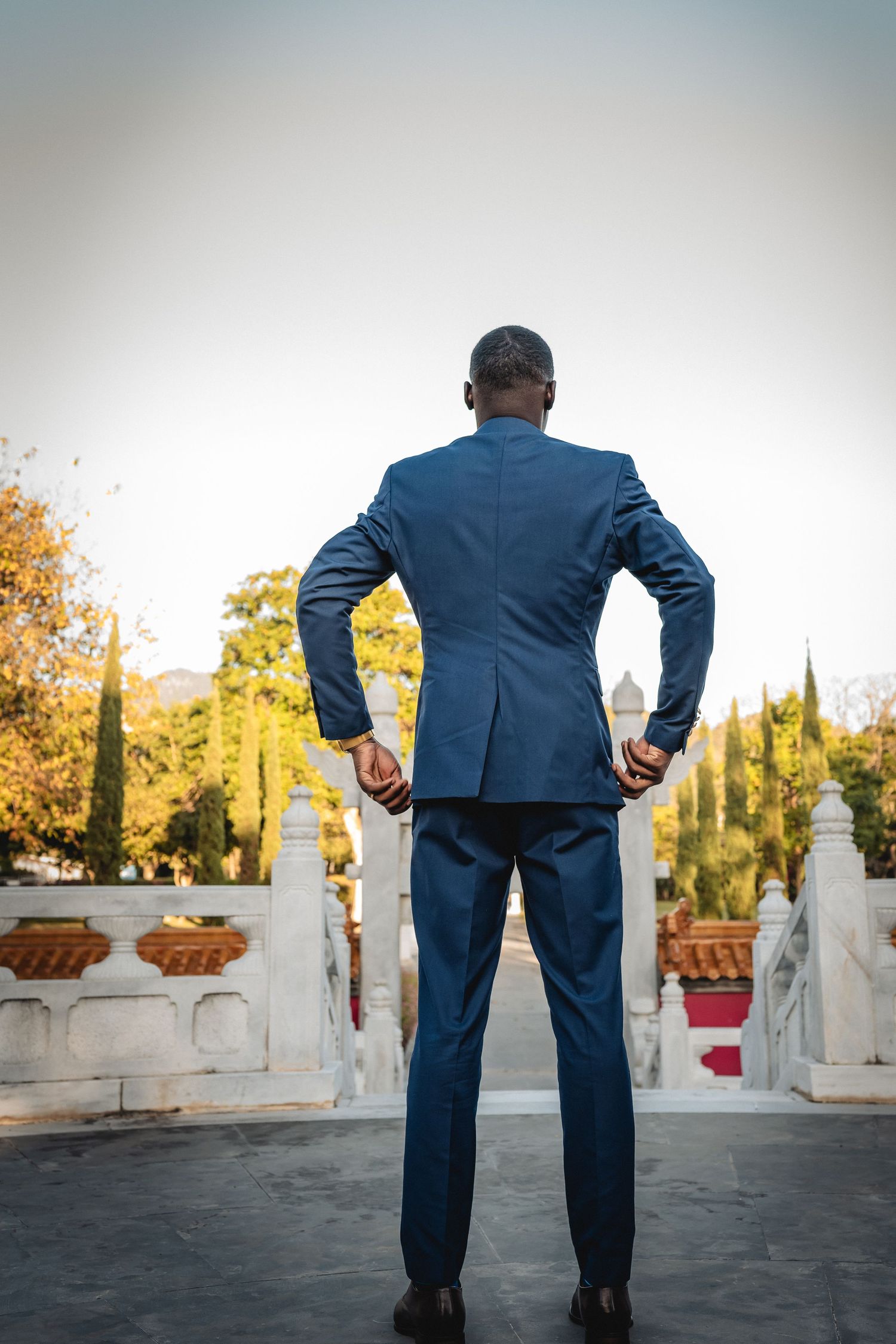 Person in navy blue suit stands overlooking outdoor venue with white architectural details.