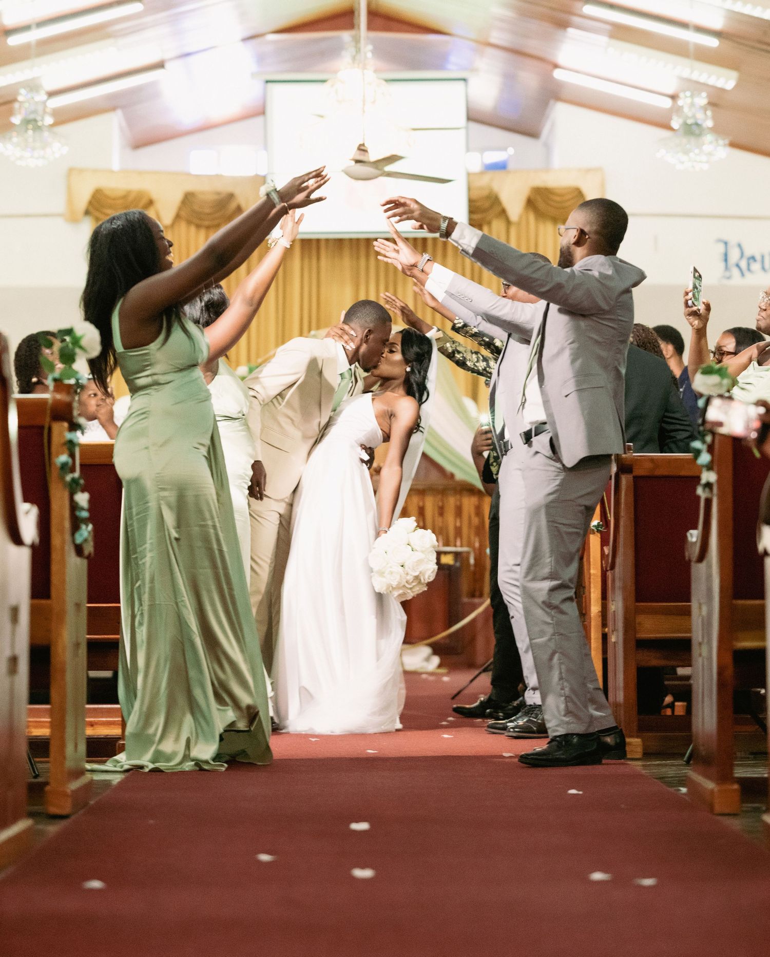 Joyful newlywed Black couple shares first kiss while walking down church aisle amid cheering wedding guests.