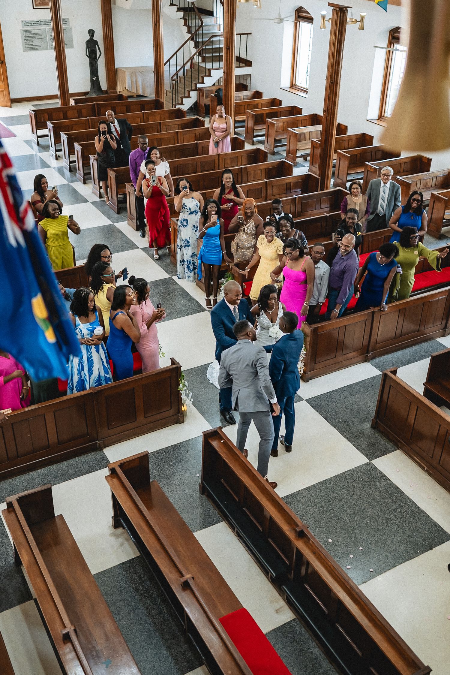 Aerial view of a wedding ceremony inside a church with colorful-dressed guests seated in wooden pews.