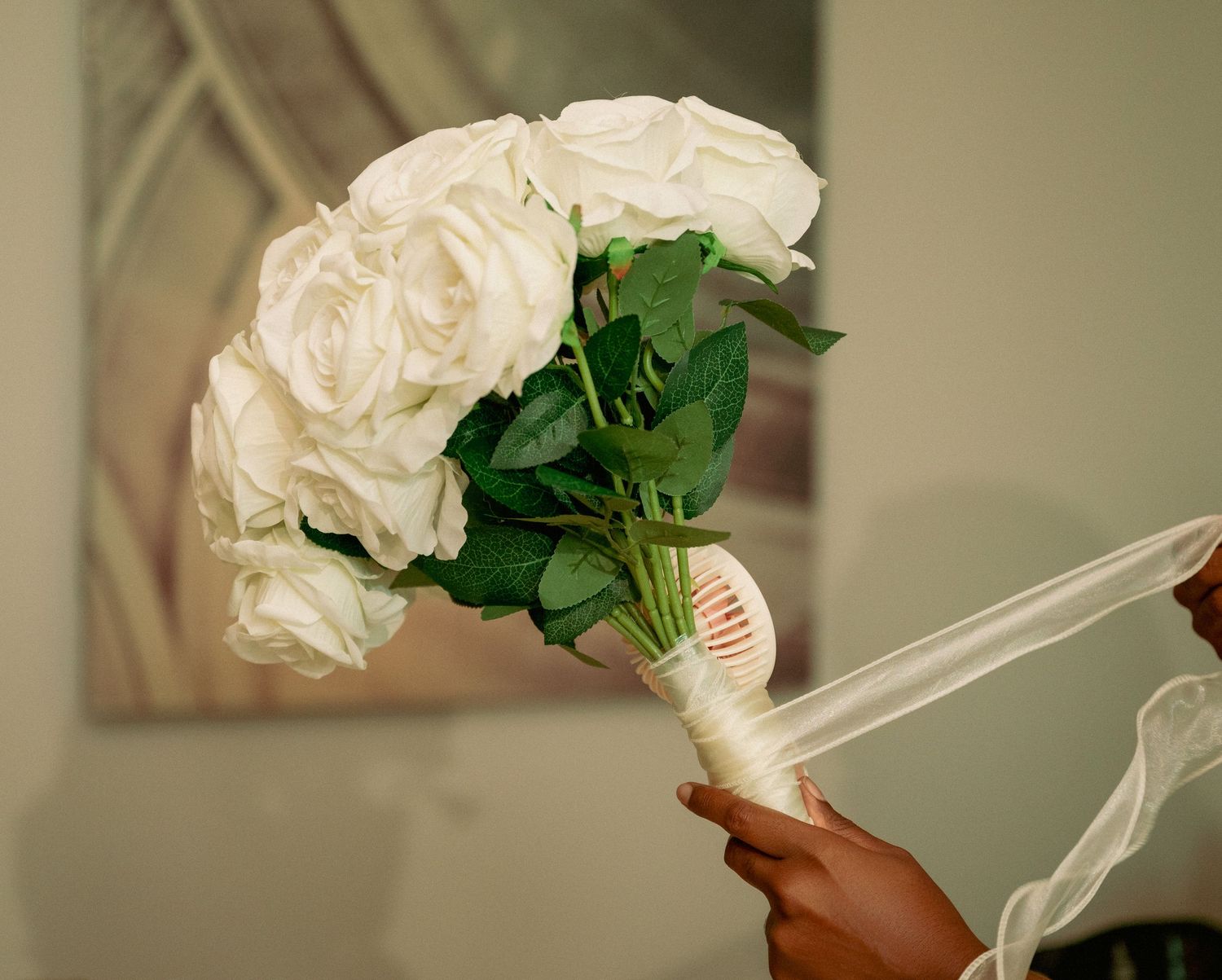 A hand holds a bouquet of white roses tied with a ribbon.