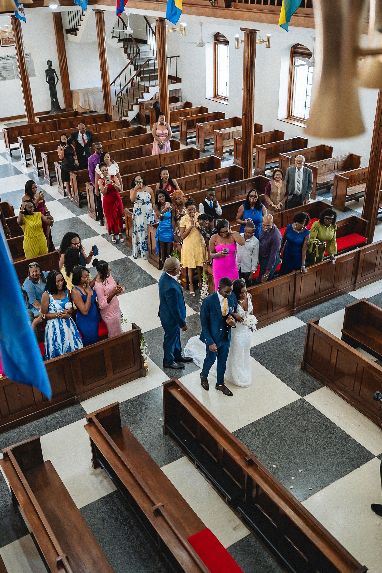Aerial view of wedding ceremony procession down church aisle with colorful guests in pews.