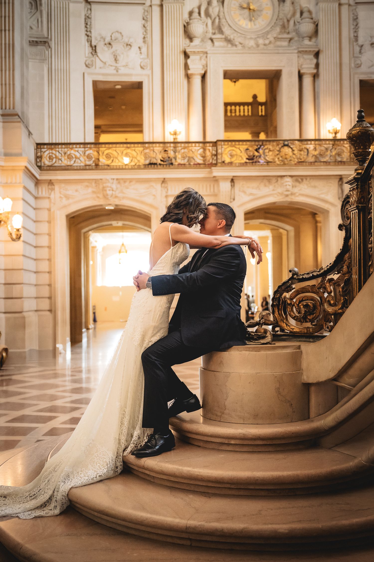 Bride and groom share a romantic kiss on ornate staircase inside elegant San Francisco City Hall wedding venue.