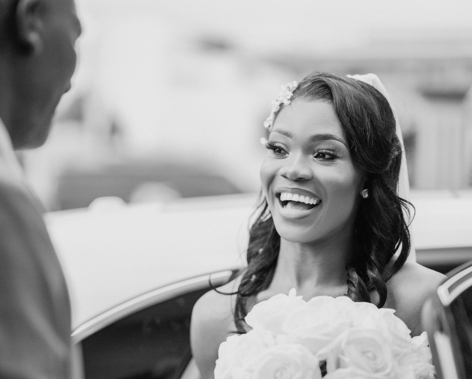 Smiling bride in white dress holding white rose bouquet in black and white wedding photo.