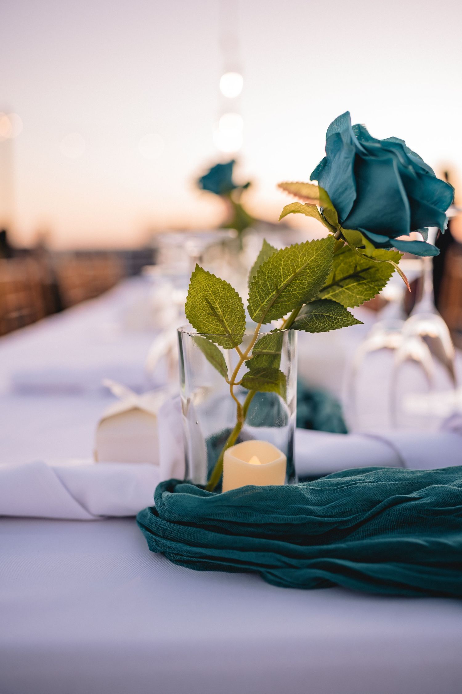 Wedding table decor featuring teal blue flowers and white linens in soft lighting.