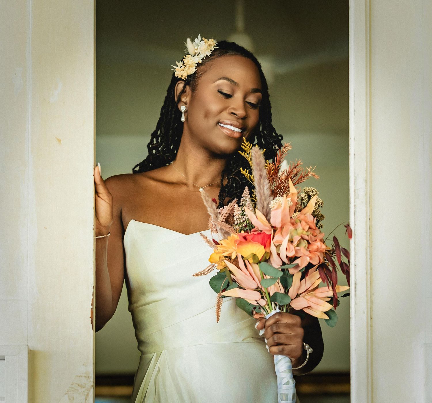A bride in a white dress holds peach and coral colored flowers against a light background.