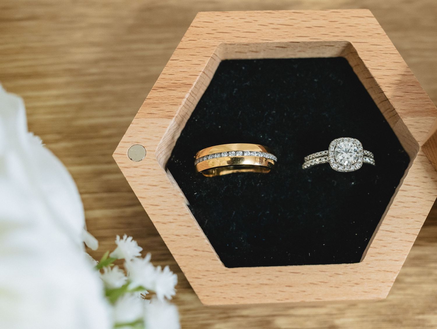 Wedding rings displayed in a modern hexagonal wooden box with black velvet interior.