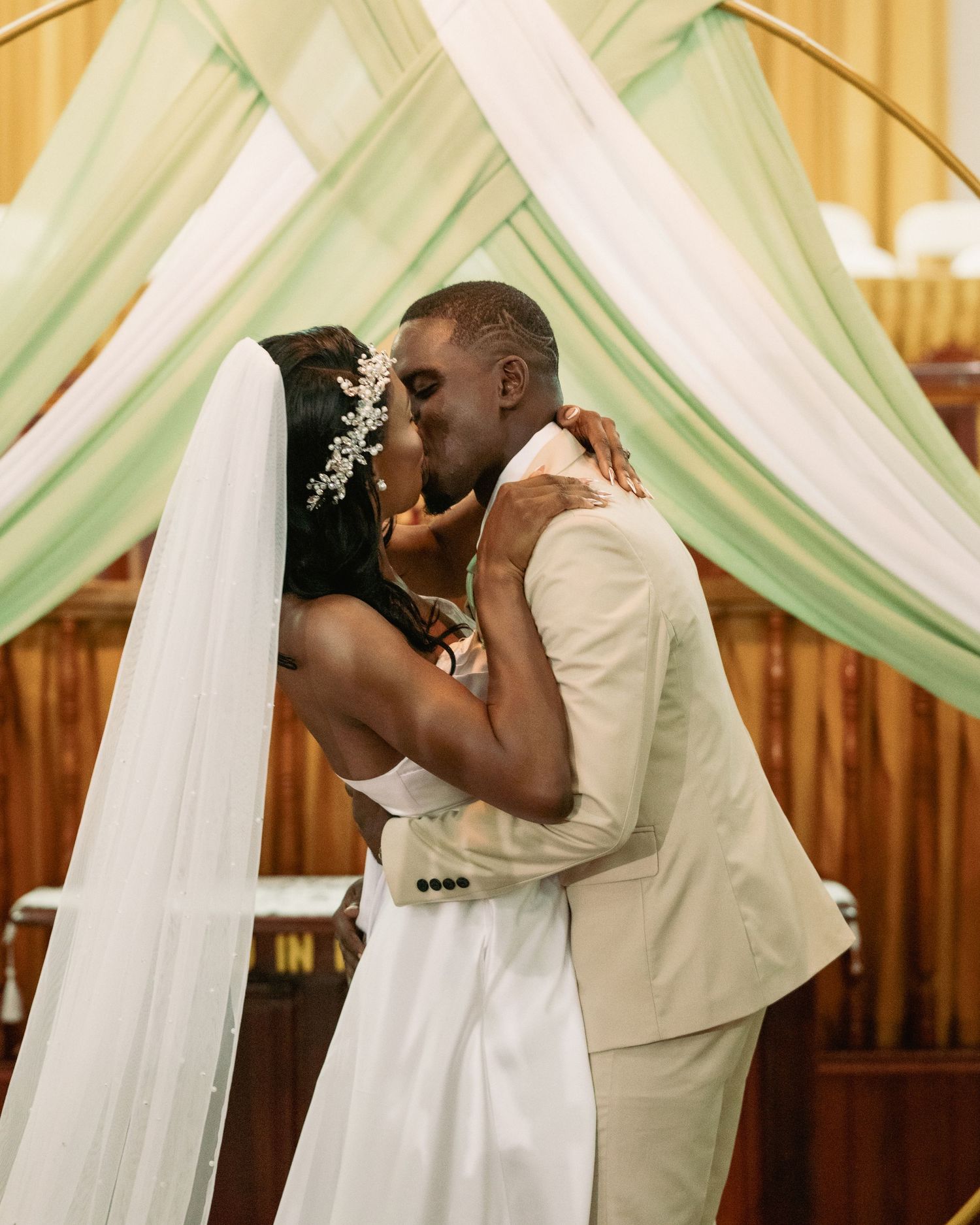 A bride and groom share their first kiss under a green and white altar arch.