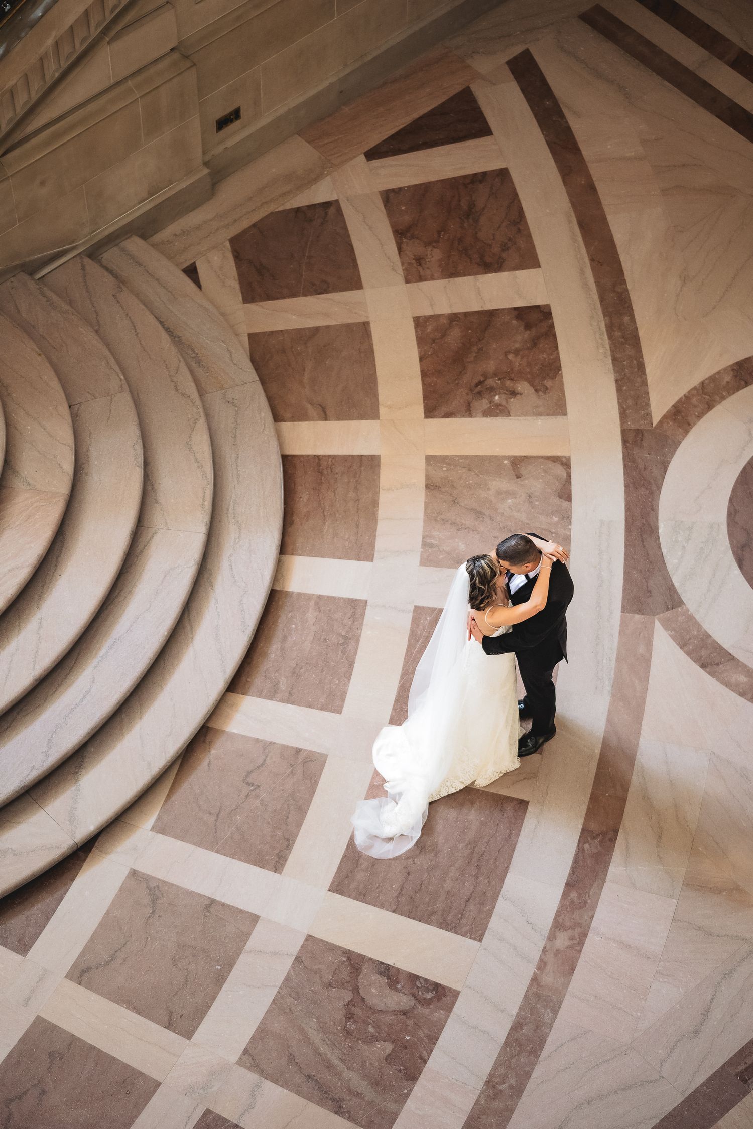 Aerial view of bride and groom sharing first dance on ornate marble floor with elegant geometric patterns.