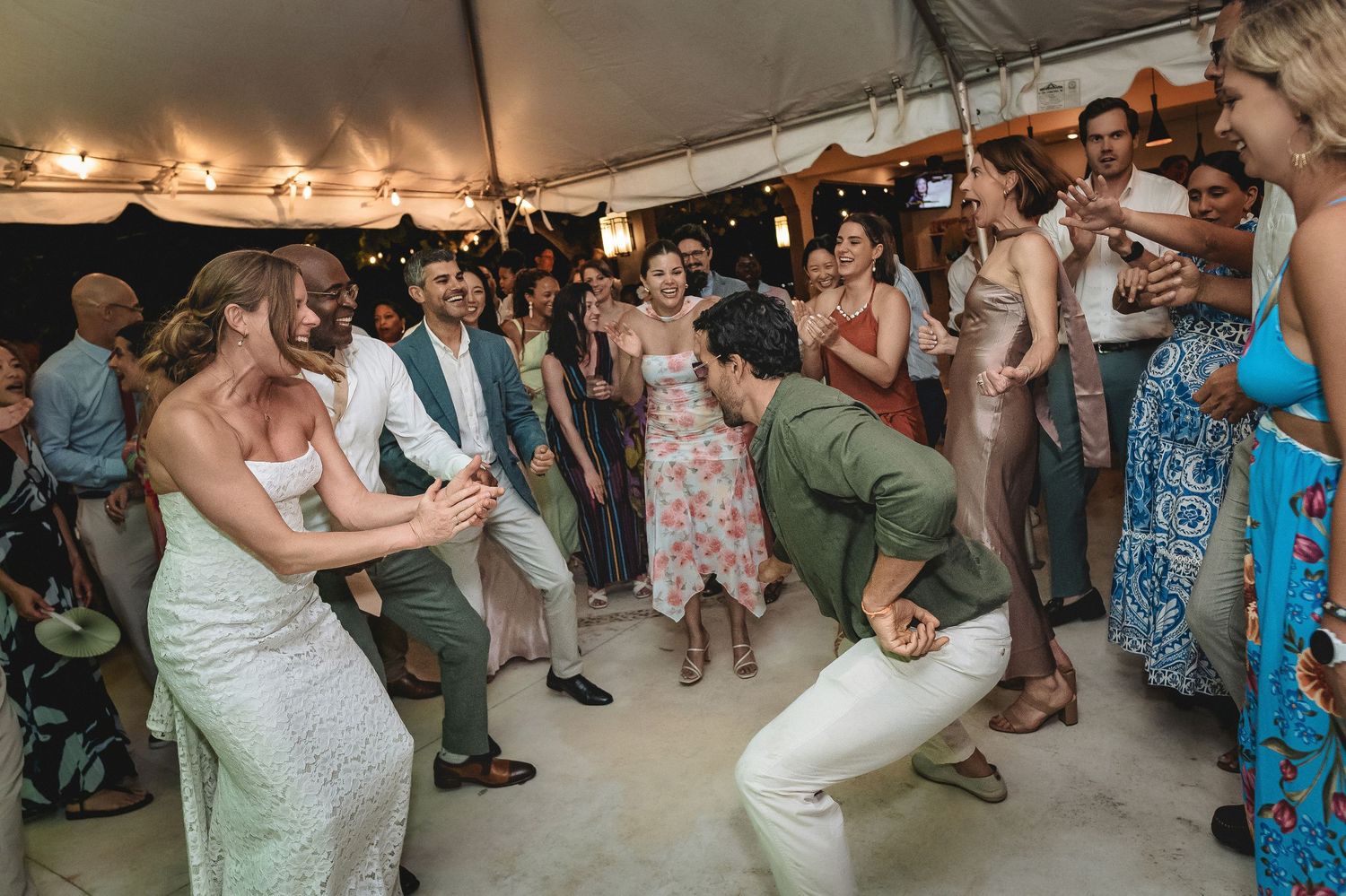 Guests dancing energetically at an outdoor wedding reception under a white tent.