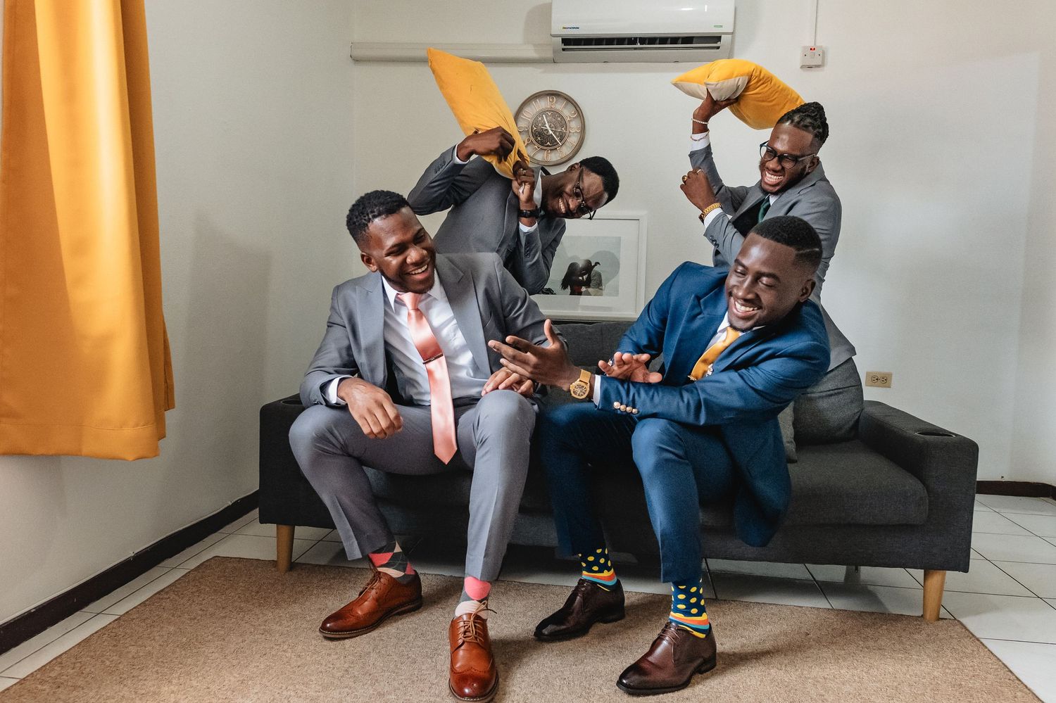 Four well-dressed men in suits celebrating joyfully on a couch, waving handkerchiefs in colorful socks.