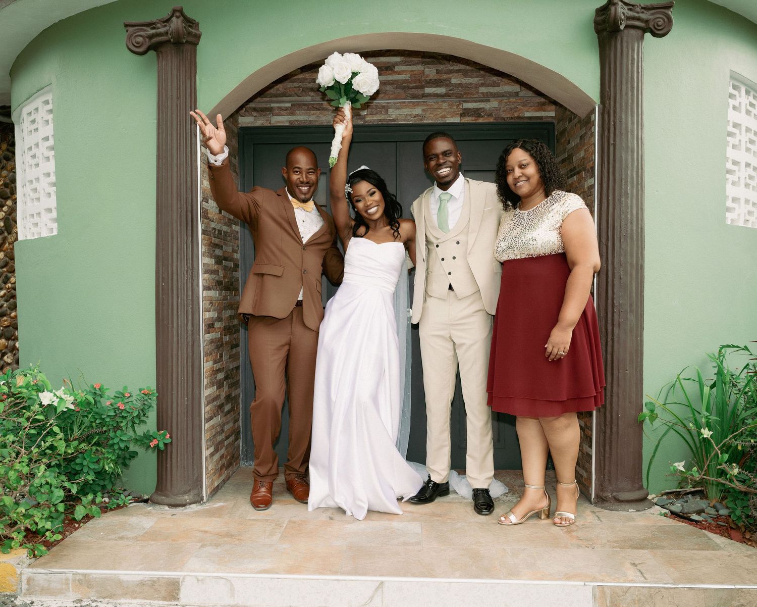 A newlywed couple celebrates with family outside a green building entrance.