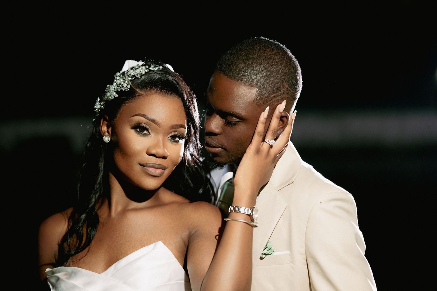 Romantic wedding couple poses intimately against dark background.